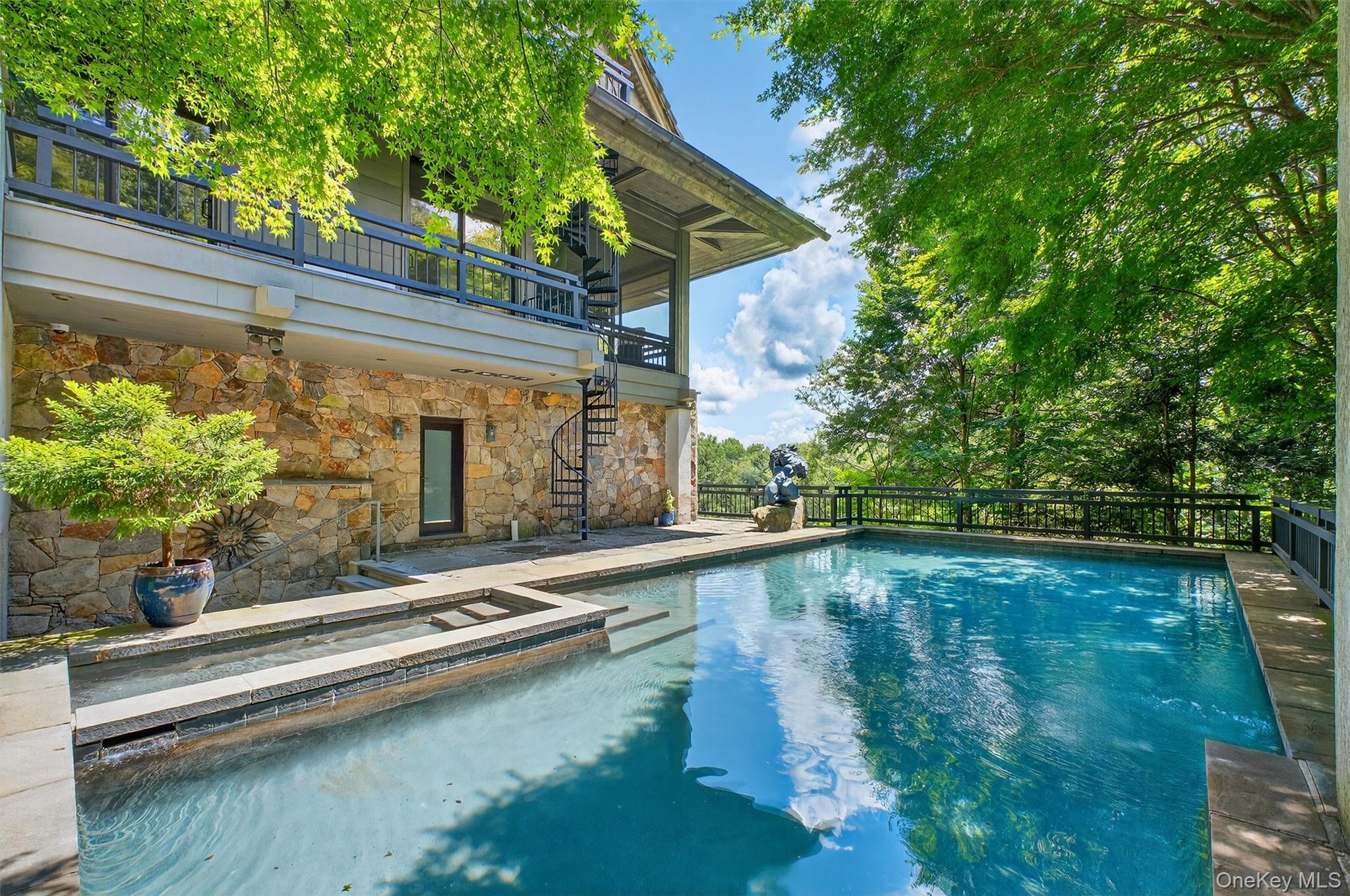 Welcome to “The Tea House” a one-of-a-kind architectural sanctuary perched above Gorge Lake in Pound Ridge, where timeless craftsmanship and natural beauty converge in perfect harmony.

Rebuilt in 1997 with inspiration drawn from the classic Japanese Tea House, this remarkable estate spans 4.79 acres of private, lakefront land bordered by the protected 738-acre Mianus River Gorge. Expertly landscaped, the property is a showcase of organic design, dramatic stonework, rare specimen plantings, waterfalls, and tranquil Japanese gardens.

The 4,712 sq. ft. main residence unfolds across three levels and offers four bedrooms and five bathrooms. The entry level opens to a peaceful suite featuring antique handcrafted doors, a fireplace, terrace access, and a luxurious bath with radiant-heated glass tile floors, sauna, and a shared shower connecting to a second full bath and the pool deck.

Stairs and an elevator lead to the second level, where a dramatic living room awaits with soaring beamed ceilings, a stunning fireplace, and walls of glass framing seasonal lake and woodland views. The kitchen, open to the living and dining areas, features custom quilted maple cabinetry, granite countertops, and a breakfast bar. French doors on either side of the living and dining rooms extend to a spacious Ipe deck and a fully equipped outdoor Viking kitchen, perfect for seamless indoor-outdoor entertaining.

This level also includes another bedroom with a full ensuite bath and private balcony overlooking the heated pool and spa, both managed by an advanced Aqualink system. Every inch of the home is thoughtfully designed to bring the outdoors in while maintaining a sense of peace and privacy.

In addition to the main residence, the estate includes two separate guest dwellings. A 1,200 sq. ft. two-level guesthouse features one bedroom, one and a half bathrooms, a full kitchen with Miele appliances, and a private driveway — ideal for hosting in style. A second guest suite, located above the three-car carport, includes a living room and full bath, while a private office space below offers a separate work environment complete with a walk-in wine fridge and half bath.

Additional features include a detached three-car garage with an air-conditioned upper level, an elevator servicing all main levels, three backup generators, radiant and hydro-air heat with over 10 zones, a Lutron lighting system, and central air conditioning and vacuum. With multiple Ipe decks, gas-fired spa and pool, landscape lighting, and lake access including a small private island, the property offers both serenity and sophistication.

Rarely does a home offer such a blend of architectural integrity, modern convenience, and emotional impact. “The Tea House” has served as a personal sanctuary — now ready to be passed on to its next discerning steward. 

Note additional out buildings bedrooms/baths and square footage: 
Cottage = 1 Bdrm 1.5 bath 570sqft
Carport = Studio + Separate office 1.5 bath 1136sqft