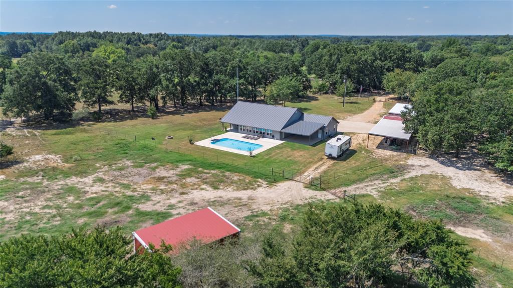 A winding drive takes you to a secluded sanctuary on a beautiful AG-exempt 21.15 acres of open land, a well-maintained home, in-ground swimming pool, workshop and more! Discover a place that is ready for livestock, gardens, or a place to unwind. Enjoy family gatherings under the large covered outdoor living space or on the oversized open patio beside the pool. Inside the 23x15 vaulted living room, a wood-beamed ceiling with recessed lights and stone gas-log fireplace creates the perfect place for nights with friends or family. The open floor plan leads to the kitchen with sleek granite countertops, custom white cabinets, island, peninsula with breakfast bar, double ovens, cooktop stove, subway tile backsplash, and stainless steel appliances. For additional living space, enjoy a 31x10 sunroom that overlooks the pool and the 50x36 open patio. Retreat to the primary ensuite with trey ceiling, ceiling fan, granite countertops, double sinks with a vanity area, separate walk-in shower, and soaking tub. With a split bedroom floor plan, the guest bedrooms share a full bathroom. Additional bonuses for this 2019-built house include energy efficient spray foam insulation, standing seam metal roof, Hardie siding, recessed lights, and luxury vinyl plank flooring. Outside, take advantage of the 20x17 metal shop building with power, 30amp RV power, 220 outlet for a welder, and water. Extra covered parking, with 112x25 feet, provides a place to park farm equipment, small tractors, cars, or etc. Sit outside and listen to the birds or watch amazing sunsets in this quiet country setting with open skies. Located just minutes from Sulphur Springs, you’re close enough for supplies but far enough away from city noise or traffic. Bring your animals and country dreams to this turn-key rural property!
