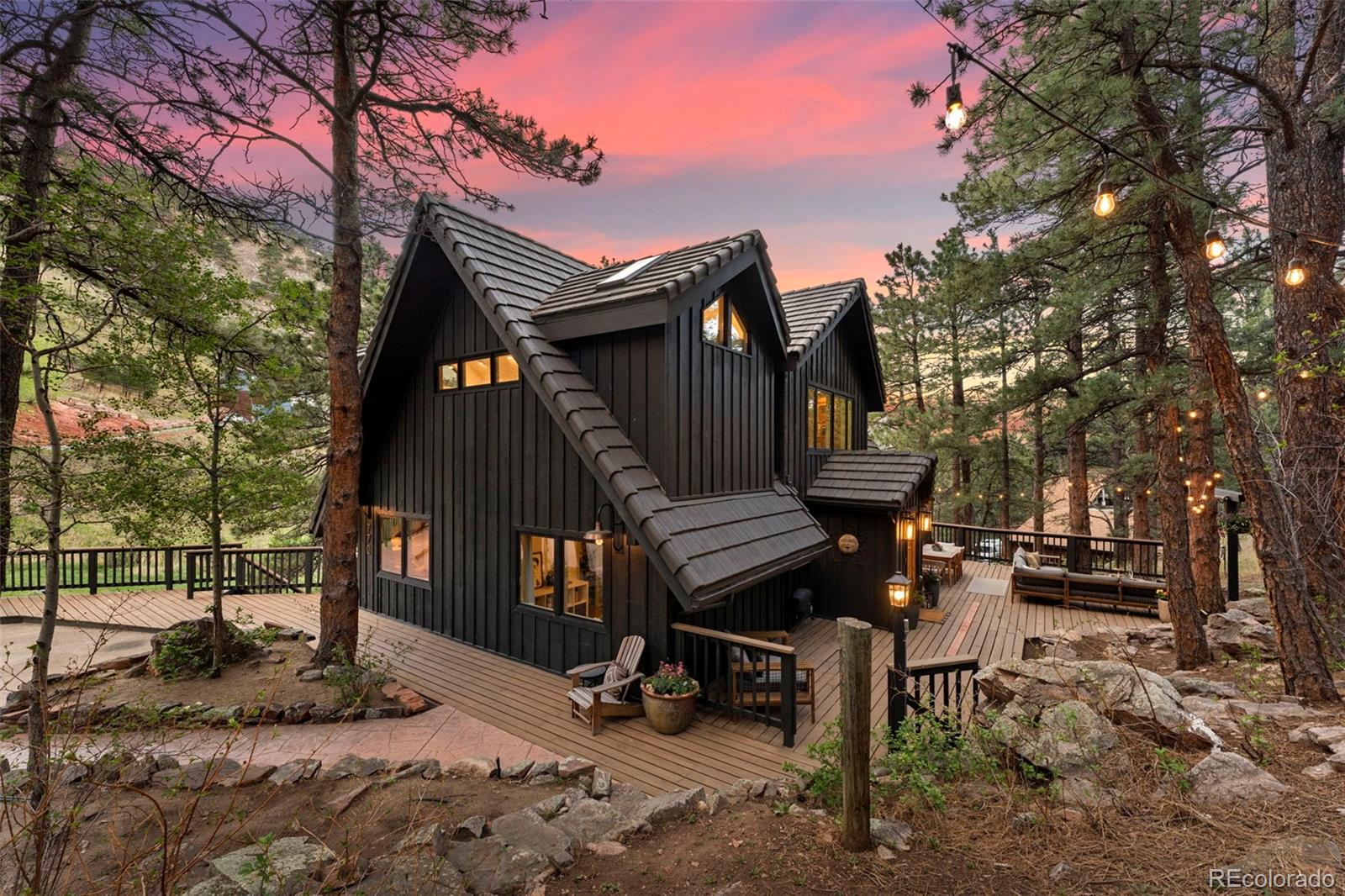 Experience the rare combination of beautifully usable acreage, extensive updates, and close proximity to downtown Boulder in this thoughtfully reimagined Pine Brook Hills retreat. Set on 1.2 acres surrounded by mature pines, dramatic rock outcroppings, and a wide open meadow often visited by deer and songbirds, the property offers a peaceful mountain setting with an easy connection to town. Thoughtfully transformed with a cohesive vision, the bright & airy interiors are grounded by white oak flooring & architectural details, curated lighting & carefully selected finishes that create warmth and continuity across the home. The vaulted main living area is crafted for both elevated entertaining and comfortable daily living with expansive windows & dual sliding glass doors opening naturally onto the wraparound deck. The kitchen balances beauty & functionality with custom cabinetry, soapstone countertops, integrated appliances, abundant storage & dedicated coffee station. A natural gas fireplace anchors the living space with warmth & ambiance. Beautifully refreshed guest spaces complete the main level while the lower level offers a private retreat ideal for multigenerational living or extended stays. Above, the primary suite provides a grand & peaceful escape with skylights, dual vanity ensuite bath with soaking tub, spacious walk-in closet with custom organization systems, private balcony, dedicated office space & loft overlooking the living area. The expansive deck is designed for memorable gatherings with a hot tub and outdoor movie screen surrounded by the quiet beauty of the foothills. Additional highlights include a detached two car garage with lower level workshop space, whole home generator, durable cement tile roof, highly regarded community water system & nearby fire protection services. A rare opportunity to own a thoughtfully transformed mountain property combining timeless style, usable land & close proximity to Boulder.