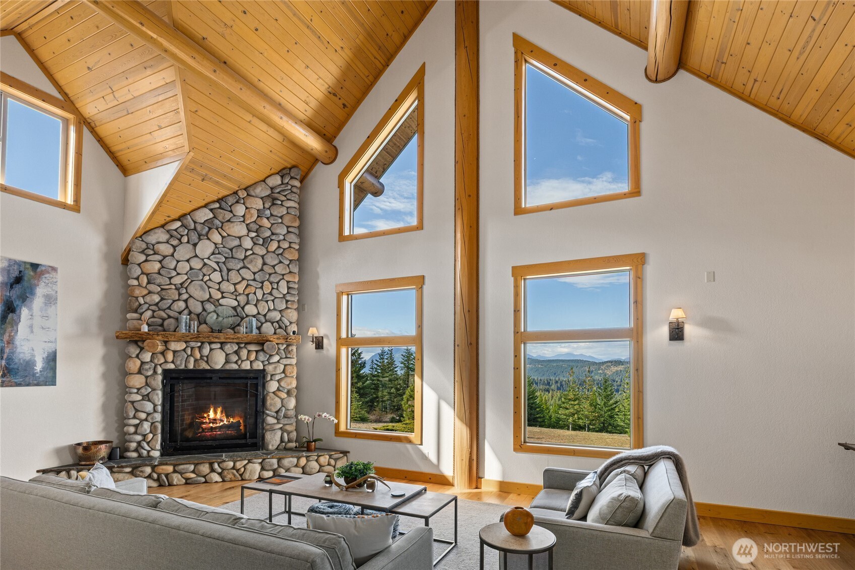 A warm blend of wood, stone, and natural light creates an inviting gathering space centered around the river rock fireplace.