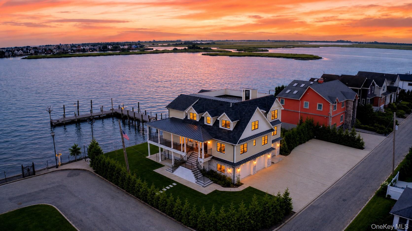 A Waterfront Lifestyle — A Private Resort Just 25 Miles from New York City 1 North Drive is a waterfront lifestyle unlike anything else on the bay.  Set on an approximately .36-acre corner parcel with frontage on both North Drive and Bayfront Drive, this exceptional new-construction home commands an extraordinary 125 feet of direct, open-bay frontage—an orientation that is rarely, if ever, available in this setting. The property has been thoughtfully designed to embrace its relationship with the water. Spectacular bay views, sunrises, and sunsets unfold from virtually every room, creating an atmosphere that feels less like a traditional home and more like a private Hamptons-style resort. Here, the water is not simply a backdrop—it is part of everyday life. THE RESIDENCEThis striking new-construction residence offers approximately 6780 square feet of total construction, with 4571  square feet of habitable interior space, complemented by a substantial wraparound deck, a full-length upper deck, and a rooftop lounge. The residence features six bedrooms, a private office, four and a half baths, and a three-bay, temperature-controlled finished garage. The garage is designed to open the entire ground level from the driveway through to the bayside, with three oversized doors creating exceptional flexibility for vehicles, storage, water toys, and entertaining. The expansive poured-in-place concrete driveway extends approximately 100 feet by 40 feet and provides extraordinary parking capacity for large-scale gatherings. The main living level is designed around the water. A sophisticated living room with fireplace flows into a glass-enclosed bayfront den, while the open-plan layout continues into a professional-grade kitchen centered by a dramatic 13-foot island finished in waterfall Carrara marble. A complete Viking appliance package includes a 48-inch range and 48-inch refrigerator, complemented by a connecting butler's pantry. The home was created equally for everyday living and grand entertaining, with a private movie theater, full gym, large attic, and beautifully appointed primary suite overlooking the open bay. The primary bath features a steam shower and freestanding soaking tub positioned to capture the waterfront views. Kohler fixtures and Lutron lighting controls throughout reflect the home's emphasis on quality, comfort, and sophisticated technology.THE WATERFRONTThe newly constructed 125-foot bulkhead has been elevated an additional 18 inches above standard height for enhanced storm protection and engineered on a soldier pile and dead-man system. Extending into the open bay is a 135-foot pier with a 20-by-20-foot dining platform, complemented by more than 120 feet of floating dock for boats and jet skis. Together, the waterfront improvements create a sheltered cove-like setting directly in the backyard, perfectly suited for boating, entertaining, swimming, and enjoying long summer days on the water.The property also features a dog washing station and Dog pen.  And Stadium flood lighting.This is a home designed for a life lived outdoors, on the water and together.  Mornings begin with sunrise over the bay.  Afternoons unfold from the docks and decks.  Evenings transition into spectacular sunsets visible throughout the house.  And throughout it all, there is an unmistakable sense of connection and place.1 North Drive is not simply a waterfront property.  It is a private resort, a gathering place, and a way of life.A private community beach is also available by membership, adding another dimension to the property's resort-like lifestyle.