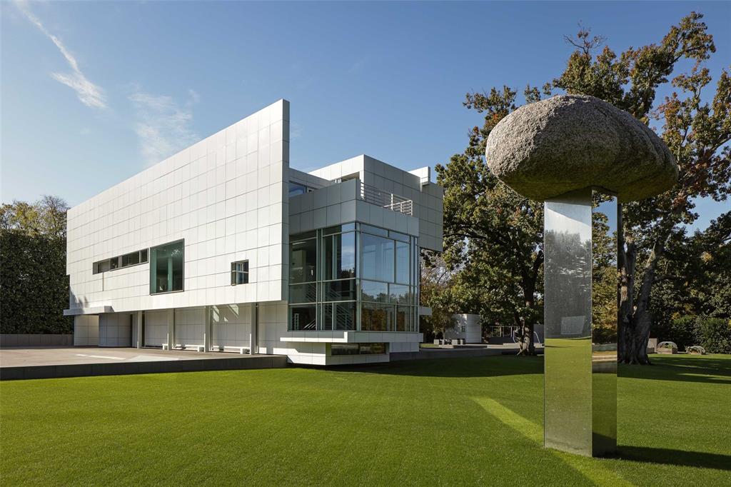 Any structure can house a work of art — only a few can become it. Designed by Richard Meier, The Rachofsky House reframes the relationship between a home and its inhabitants. This iconic Dallas residence is an invitation to realize beauty, to explore abstraction, and to become, in a quiet way, part of its evolving composition. Meier's characteristically white, metal-paneled house appears almost suspended above a black-granite podium. Beyond, ancient oaks and a gently sloping lawn frame a lagoon-like pond. '[The house] unfolds as a kind of procession through a series of zones,' says Meier, 'taking one from the outdoors to indoors, and then back outdoors again…grass, trees, pond and sky are visible from every angle of the house.' From the entry gallery, you move past a glass-enclosed stairwell toward the dining area, where floor-to-ceiling windows reveal a lush, evolving backdrop. Volumes open into one another: a soaring double-height living room, a removed primary suite, and a suspended study overlooking the grounds. Outside, a black granite patio, reflecting pool, and private lake extend the architecture into nature, blurring where dwelling ends and landscape begins. And yet, it is light that emerges as the home's most profound guide. As the day unfolds, sunlight moves through the space like a steady docent — casting shadows, illuminating details, and transforming familiar rooms into living, changing forms. More than a feat of architecture, the Rachofsky House is attuned to the understated rituals of daily life, delicately balancing public grandeur and private intimacy. As Meier himself reflected, 'the purpose of the house is to provide a place of residence and respite…a catalyst for further contemplation of nature and art, and the science of bringing them together in harmony.' When art is so often meant to be admired from a distance, the Rachofsky House invites you into the frame — tempering the boundary between observer and masterpiece.