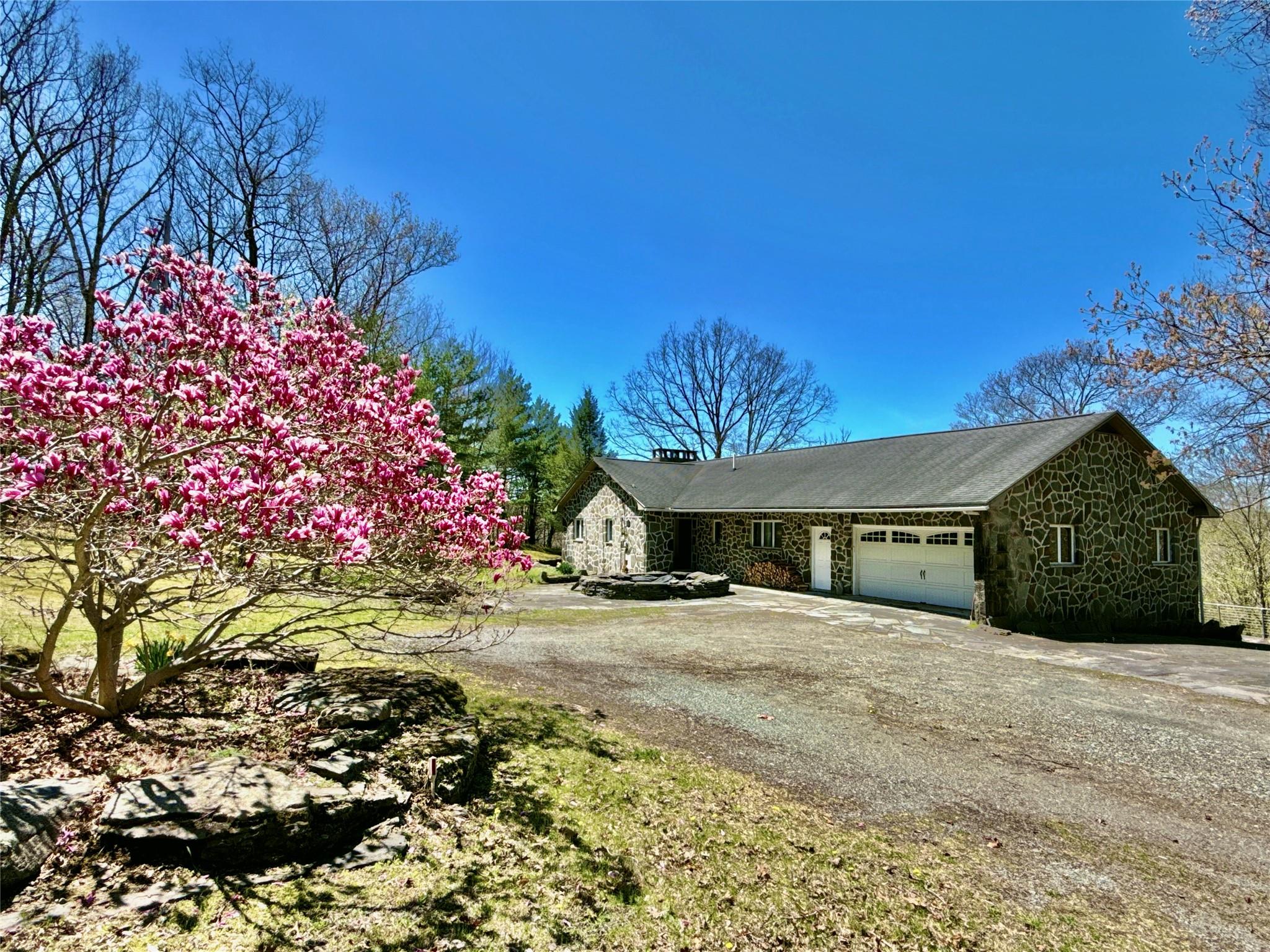 View of front facade with a chimney, a garage, driveway, and stone siding