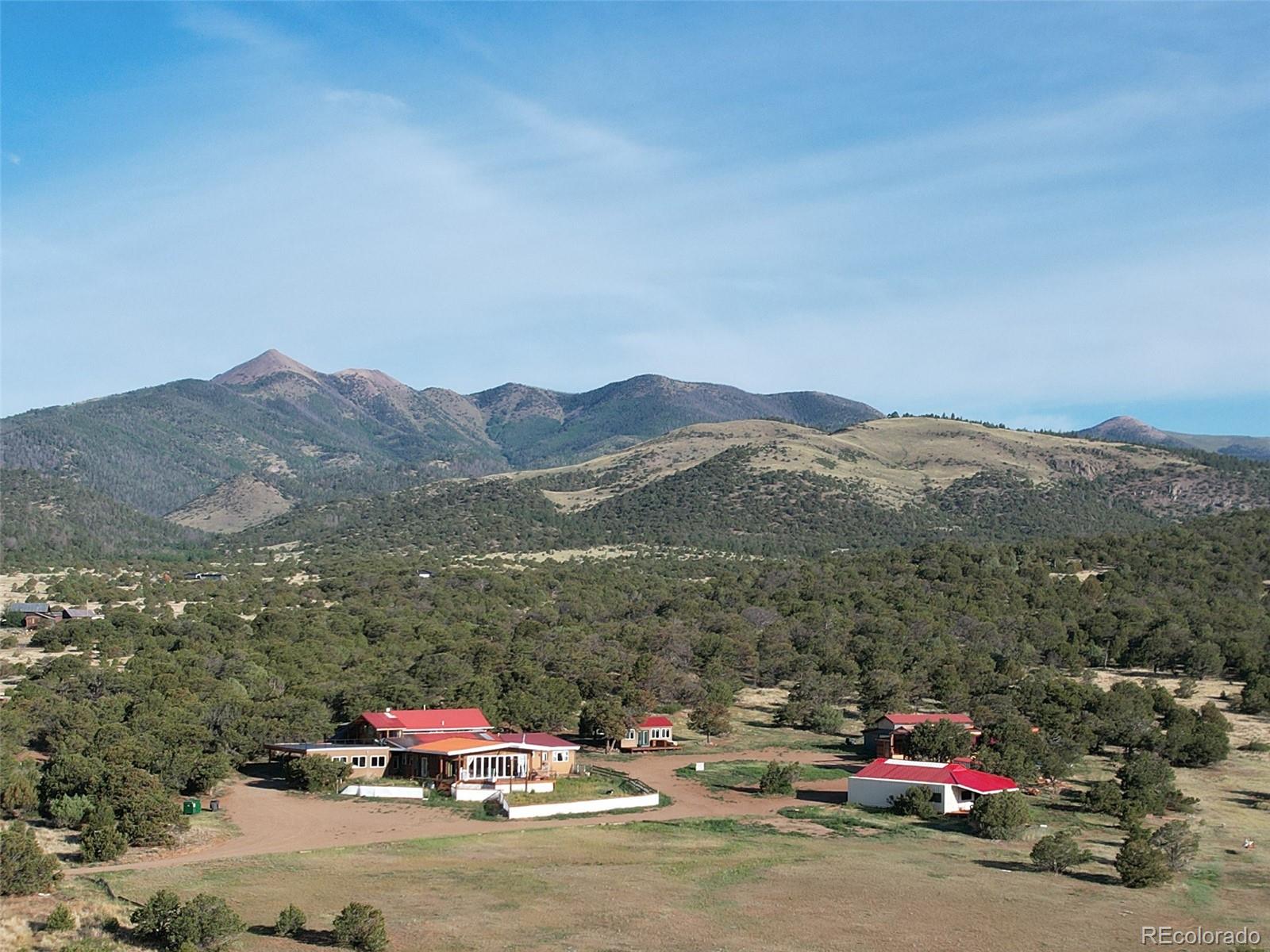 This spacious contemporary home complex has it all and will inspire your mountain living dreams. The property sits in a well-established dark skies area that features incredible views of the Sangre De Cristo Mountains. The main house is a sizeable 3285 feet and includes a small separate apartment that can produce income as a short term rental, long-term rental, or guest quarters. 
The lock-off apartment sits atop the main home with its own staircase and incredible deck. Imagine living in quiet seclusion and yet only 35 minutes from Salida and just 5 minutes to the historic town of Villa Grove. Enjoy high-altitude sunshine, no covenants, and access to the National Forest and BLM for all your recreational and hunting desires (game unit 681). Privacy abounds with juniper stands on three sides and an open meadow complete with a fenced horse arena to the east. Entering the home from the covered carport or the front door, you are swept into a sun-drenched open combined kitchen, dining, and living area that provides expansive views across the valley. A wall of glass doors opens onto the front deck, complete with an outdoor fireplace, perfect for those small, intimate evenings or grand enough for large gatherings and family get-togethers. The kitchen features stainless appliances and colorful backsplash tiling. The primary bedroom opens to another smaller front deck that looks out over this beautiful property. Just off the kitchen and sun room, you will find a lovely front raised bed garden area just waiting for your vegetables and herbs. A separate she shed with a deck is ready to go, and two other outbuildings provide ample room for toy and vehicle storage. One of these is a barn with separate workshop and office.  Three are three 40 foot storage containers tastefully tied in to make for more storage or expansion space.  Come see this hidden gem priced well below appraisal price.