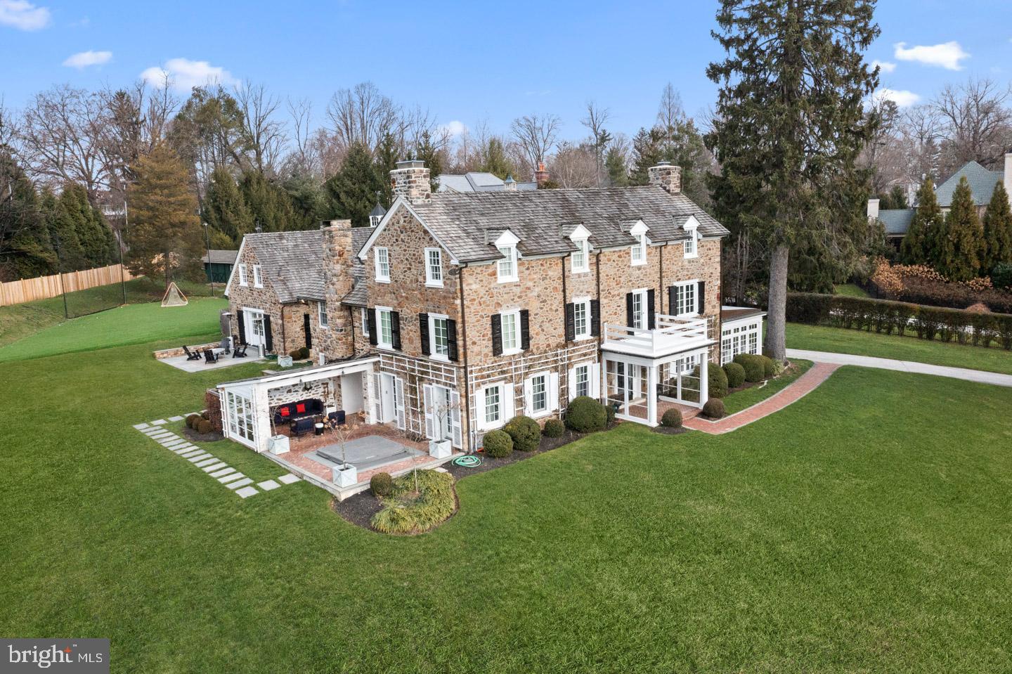 This Federal style fieldstone residence known locally as The Spring House stands proudly atop 2.1 manicured hilltop acres in Radnor School District. With its elevated presence, classic fencing, and visually prominent corner setting, the home makes a striking first impression while offering privacy and distinction. Spanning approximately 5,500 square feet across three gracious levels, the main residence features five bedrooms and five and one half baths. In addition, enjoy a separate one bedroom, one full bath guest cottage. A detached garage is made up of two bays, a climate controlled peloton room/gym and an extensive weight room. The turf field with stadium lighting, putting green, in ground pool, separate hot tub, and generous recreation areas are designed for both intimate gatherings and large scale entertaining creating a truly special estate lifestyle. Steeped in history yet thoughtfully modernized, the home blends original architectural character with contemporary refinement. Reclaimed hardwood floors, exposed beams, and dramatic stone walls preserve its heritage, while extensive renovations, including a newly renovated kitchen and guest cottage, ensure effortless modern living. The gourmet kitchen serves as the heart of the home, centered around a 10 foot island with farmhouse sink and striking 4 inch quartzite countertops. A charming built in window seat provides additional kitchen table seating and overlooks a picturesque courtyard framed by a stone wall and architectural ivy lattice. The open Butler’s pantry with beverage refrigerator adds both function and elegance. Premium appliances include a BlueStar French Blue double oven with commercial grade six burner and griddle cooktop and custom hood, oversized Miele refrigerator and freezer, built-in Miele coffee system, Wolf warming drawer and microwave, and two Bosch dishwashers. White cabinetry with elegant silver hardware, built in pantry shelving, reclaimed hardwood floors, and classic subway tile complete the timeless design. The family room is warm and inviting with reclaimed hardwood floors, a beamed ceiling, and a striking stone wall. Built-in bookshelves and cabinetry provide both charm and storage, while a gas fireplace, the first of three in the home, anchors the space. Three French doors open to the side covered patio with hot tub and courtyard creating seamless indoor outdoor flow. The living room features a second gas fireplace with a white brick surround, designer wallpaper, and impressive deep windowsills. Two French doors open to the patio, while double doors lead directly to the foyer. The dining room showcases designer wallpaper and an 18 inch deep windowsill. Two sets of glass doors lead to the sunroom, enhancing the home’s natural light and flow for entertaining. The sunroom is a light filled retreat with three walls of windows and brick flooring. A suspended sofa adds a distinctive architectural focal point and relaxed elegance. Upstairs the bright primary suite is a private retreat featuring dual baths and dual walk in closets designed by California Closets. Two bedrooms, one full bath with a steam shower and the laundry room complete the second floor. The third floor oasis has the fourth bedroom with an en suite full bath, the fifth bedroom, the fifth full bathroom and a large storage closet.  Located in the highly sought after Radnor School District and close to most private schools, the lifestyle is equally exceptional. Enjoy walking access to the Radnor Trail, downtown Wayne’s shops, restaurants, train station, and the spectacular gardens of Chanticleer. Major commuter routes provide convenient access to Center City Philadelphia and beyond. A rare opportunity to own a landmark Main Line estate where enduring history, architectural beauty, and modern luxury converge.