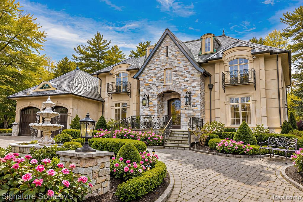 Directly across from Quarton Lake with unobstructed water views, this 4-bedroom, 5.2-bath residence with a first-floor primary suite offers 4,912 sqft in one of Birmingham’s most coveted settings. Designed with an appreciation for artistry and scale, the home opens to an 18-ft two-story foyer with a sweeping curved staircase and bronze and crystal chandelier, establishing an immediate sense of grandeur.The living room rises to two-story heights, framed by dramatic windows and centered around a gas fireplace. Architectural moldings, carved ceiling motifs, and an open balcony above add depth and connect to the second level. An appointed dining room features a tray ceiling with hand-painted scenes and French doors to the bluestone patio for seamless outdoor entertaining. A private den offers an intimate retreat with hand-painted cloud ceilings, gold stenciled cherry blossom finishes, and custom cabinetry. In the kitchen, white Wood-Mode cabinetry with gold and crystal hardware pairs with porcelain countertops, a sculptural island, and professional-grade appliances. A wall of glass overlooks the bluestone path to the private backyard. The main-floor primary suite includes two walk-in closets and dual marble baths—one with a Jacuzzi tub, the other with a marble shower. Three additional upstairs bedroom suites offer walk-in closets and private baths with updated quartz counters and fixtures.Outdoors, professionally designed landscaping includes a heated brick paver driveway, bluestone entry, limestone fountain, and a rose garden with 339 bushes. The backyard offers a private setting with a bluestone patio, built-in fountain, and mature landscaping for both quiet use and entertaining. Throughout, custom oak flooring, extensive crown moldings, and curated lighting are paired with a whole-house generator, snow-melt systems, and advanced HVAC—bringing together craftsmanship, comfort, and enduring architectural design.
