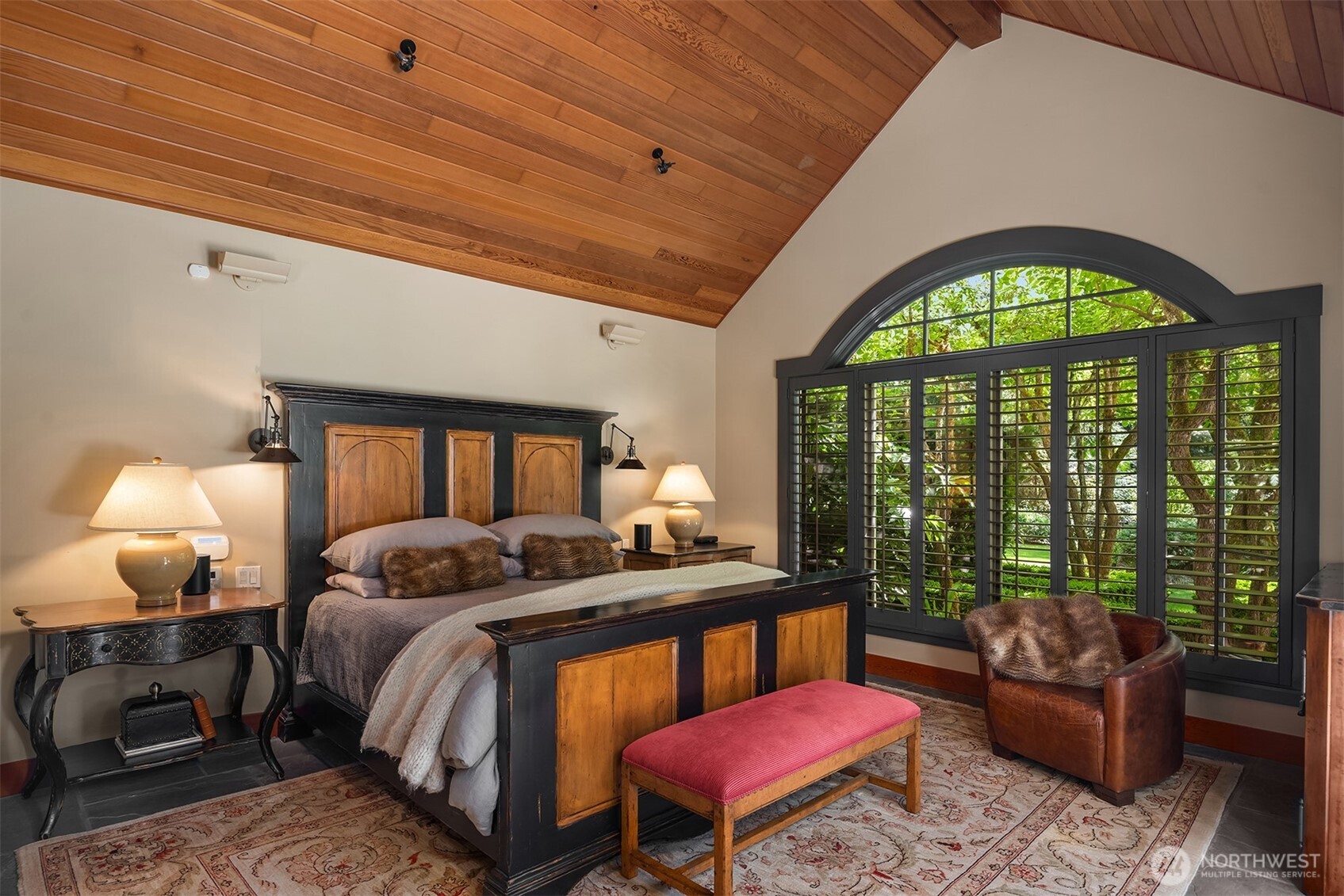 Primary bedroom with dark wood bedframe and arched shuttered window