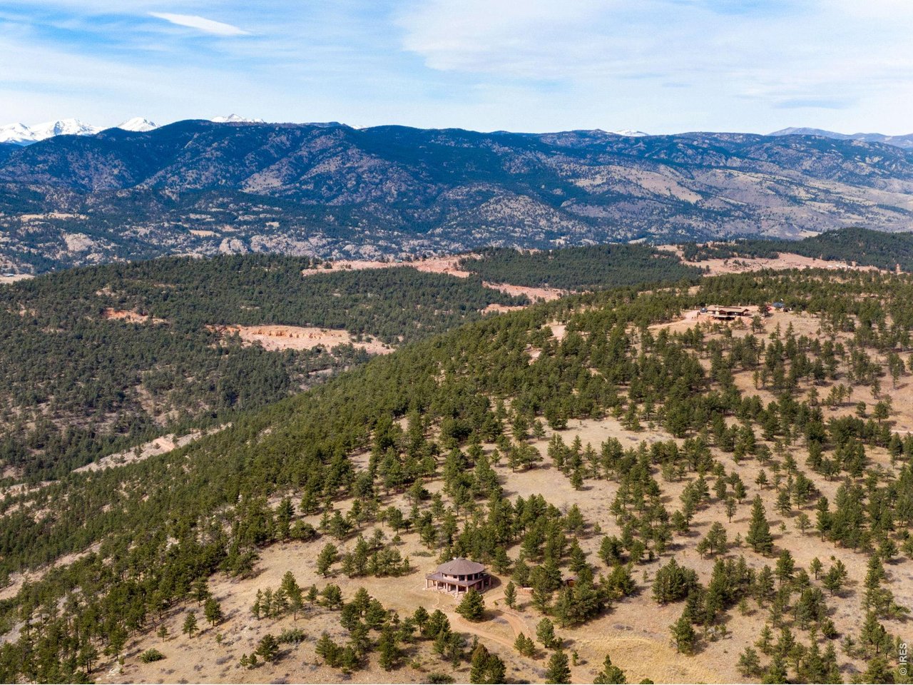You'll be amazed by this extraordinary architectural gem on 10+ acres in the scenic foothills above the Town of Lyons and overlooking the entire Lyons valley and the mountains beyond, all the way to the Continental Divide. If a spectacular view is your jam, this is the one! This remarkable property stands apart with its 15-sided structure, offering a one-of-a-kind home designed to capture light, views and serenity from every angle. From the moment you enter, you'll appreciate the thoughtful layout and unique form. The entire top floor is open to allow for the 360 view, creating an unparalleled living experience that feels expansive and connected to the landscape. With windows on all sides for fabulous flow-through ventilation, the design brings the outdoors in, bathing the interior with natural light and refreshing breezes year-round. This custom home blends rustic charm with modern comfort, anchored by a soaring central space that is naturally inviting and ideal for both everyday living and entertaining. The open-concept floor plan enhances the circular flow, embracing the panoramic vistas that stretch to the Rocky Mountain peaks and beyond. Outdoors, discover nearly new composite decking that wraps portions of the home, providing durable, low-maintenance outdoor living areas perfect for lounging, dining, or simply taking in the tranquil surroundings. Additional features of the land include unmatched privacy, plenty of relatively flat and quite usable acreage, and abundant solar exposure, mature trees, a sweet 11x10 log studio building, and proximity to natural recreation while still being close to the amenities of Lyons, Longmont and the St. Vrain Valley community. With its blend of distinctive design and dramatic views, this property truly stands out as a rare and special offering! Generac whole house backup generator also included. Eagle Ridge Land & Homeowner's Association fee is $550/year for road maintenance.