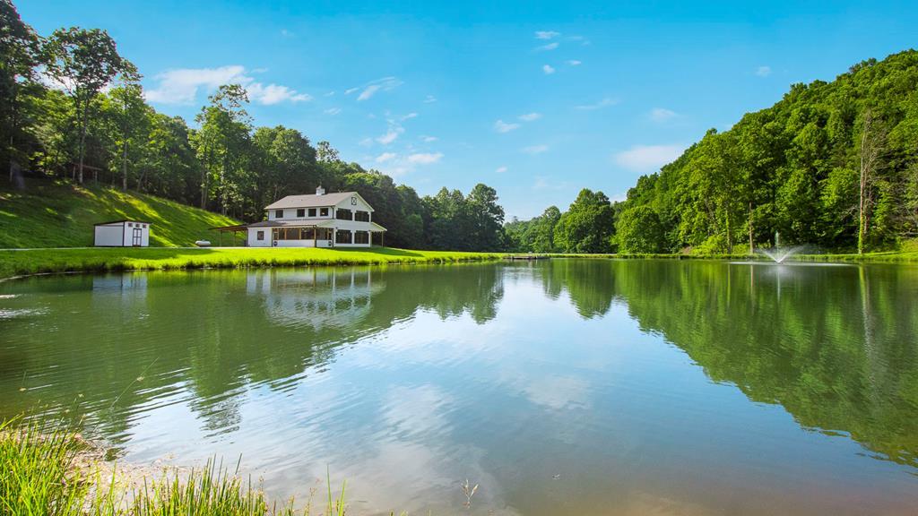 Imagine stepping onto a breathtaking 140.89-acre unrestricted mountain estate in beautiful Nantahala NC. Fresh mountain air mingled w/wildflowers greets you, as gentle waves lap the shores of a private stocked pond. Dip your fingers in cool water, cast a line & watch fish leap under sparkling sunlight reflections. In the 2024 built barndominium (2,229 sq ft, 3 beds, 2.5 baths) sunlight floods an open floor plan, framing serene pond & mountain vistas. A lovely, stacked stone fireplace crackles invitingly; the kitchen & dining area enhances every meal with peaceful views.  A main-level primary suite provides quiet luxury; two upstairs bedrooms, bonus loft room, & a full bath complete the cozy home. +/-15 acres of fenced pasture is ideal for horses grazing. Own 25-30 acres of wooded ridge line in deep greens and shadowy blues feature peaceful trails winding through the trees. Rolling hills & open views offer stunning mountain views shifting from misty dawn purples to vibrant autumn crimsons. Screened patio & covered porch extend living outdoors—feel the soft evening air, hear frogs chorus at dusk, watch fireflies dance over rippling lake. Complementing the main houses is the rustic "old charmer" guest house (4 beds, 1 bath), exuding nostalgic warmth—perfect for family, guests, or creative escapes. Outbuildings enrich the estate: barn with hay loft, attached chicken pen, equipment shed, new storage building, livestock sheds, plus a garden—all nestled naturally. Abundant wildlife (deer, bear, turkey & squirrels) affirms true mountain serenity, with trails for hiking, 4wheeling, and adventure near Nantahala National Forest, the Nantahala River rapids, & the pristine Nantahala Lake. This rare gem awakens every sense: chill pond water, whispering ancient trees, homegrown bounty, profound starlit peace. Awaken to misty mornings, harvest under vast skies, gather by crackling fire. Not just property—a full-sensory immersion in NC's wild heart. Schedule your private tour today!