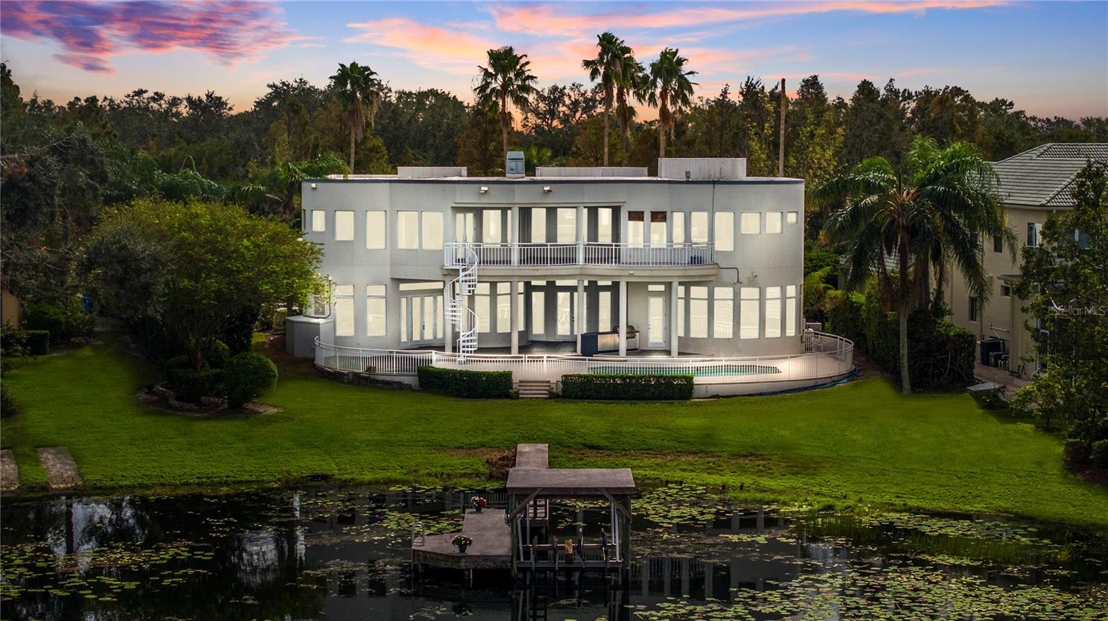 Discover LUXURY LAKEFRONT LIVING at its finest in this nearly 6,000-square-foot custom estate on the shores of skiable WHITE TROUT LAKE. Nestled within the exclusive gated community of The Estates at White Trout Lake, this exceptional residence offers 111 FEET OF PRIVATE LAKE FRONTAGE, nightly sunsets, and direct access to one of Tampa’s most coveted lakes for motorized boating and water recreation. CUSTOM BUILT by renowned ALVAREZ HOMEBUILDERS, this thoughtfully designed home blends timeless craftsmanship with flexible functionality—original builder plans are available for review. Inside, soaring 22-FOOT CEILINGS, coffered detailing, crown molding, and expansive windows showcase spectacular lake views and invite natural light throughout.The gourmet kitchen features solid wood cabinetry, stone countertops, a convection oven, cooktop, wine refrigerator, and dual pantries—perfect for the culinary enthusiast. A grand formal living room, dining room, private office, GAME ROOM WITH WET BAR, and multiple bonus spaces create versatile options for work, play, and entertaining. Upstairs, the private primary suite is a serene retreat with its own gas fireplace, morning bar, spacious walk-in closet, spa-inspired bath, and a private balcony overlooking the lake. Outdoor living is elevated with an oversized screened lanai, summer kitchen, sparkling in-ground pool, and a private dock with composite decking, boat lift, and a second-level viewing platform. Significant updates include new LUXURY VINYL PLANK flooring, fresh interior paint, updated lighting, and two newer HVAC systems (first level). A new SILICONE WATERPROOF ROOF COATING was installed on the entire roof and all parapet walls in April 2025, providing added peace of mind and long-term protection. The spacious laundry room includes a built-in pet-washing station, and the 3-car side-entry garage with circular driveway ensures ample parking. Located just 15 minutes from downtown Tampa and convenient to upscale shopping, dining, and top-rated medical facilities, this stunning lakefront property offers the perfect blend of privacy, elegance, and lifestyle. No CDD fees and low HOA dues complete the package—WELCOME TO YOUR PRIVATE LAKEFRONT SANCTUARY.