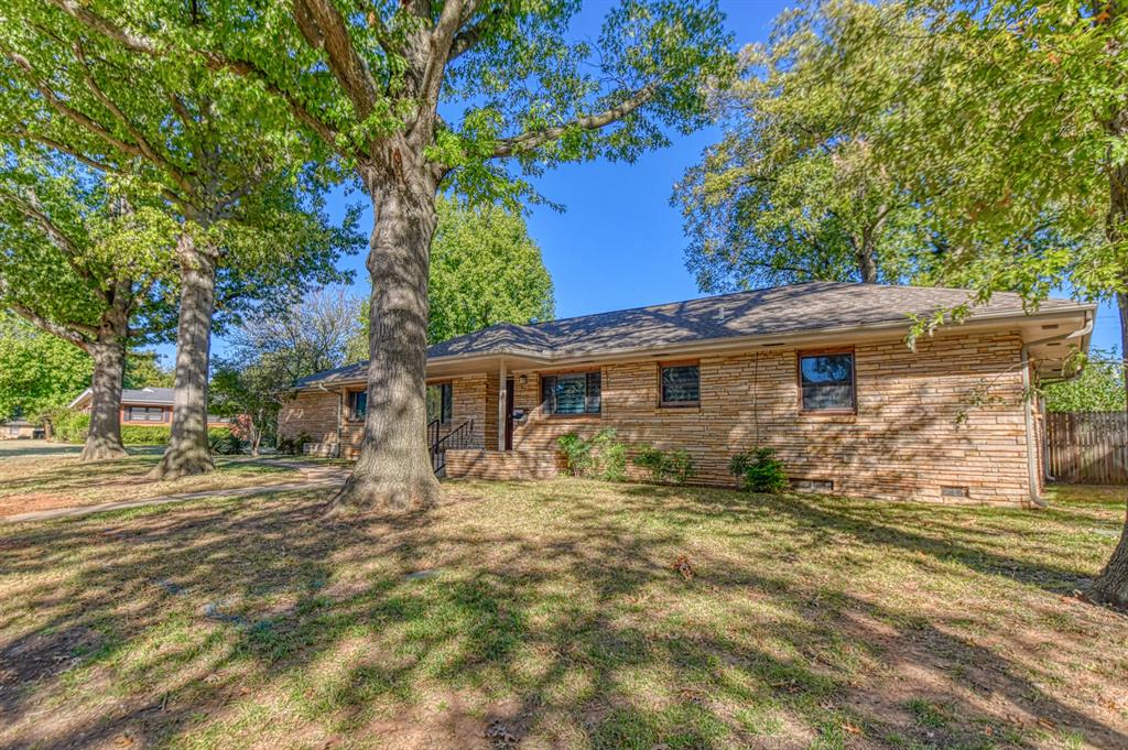 Charming home on an over-sized lot with tons of mature trees and located within just a mile from OU campus! The detached garage is set up with electricity, has a 2-vehicle carport added to it, and overlooks a huge driveway with more than ample parking space! The nice-sized, covered porch provides a welcome feel with room for a sitting space! The back patio opens to a huge yard with possibilities galore!  Stepping inside, you are met with a tasteful mix of vintage and contemporary styles! The front room may serve as both a formal dining /living room, depending on your specific needs! The kitchen is partially modernized with updated countertops and fixtures while offering tons of cabinet space, a little desk for the laptop, and breakfast nook for casual dining!!  The central living room comes with a cozy wood-burning fireplace, built-in bookshelves, and natural lighting from the large picture window! That room and all 3 bedrooms come with hard-wood flooring. The bathrooms come with classic style, colorful tiling and tub/shower combos. The carpeted extra living area has a ton of closet space, is great for a den/TV room, and allows access to both the back yard and driveway! For added convenience, the home does come with an underground sprinkler system! Updated electrical, plumbing fixtures, and windows help the energy efficiency! This home is a true gem and hard to pass up, so schedule your tour ASAP!!