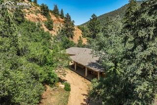 Where timeless design meets natural beauty, this exceptional home offers peaceful mountain living on a private, wooded lot. Thoughtfully updated, it blends classic architecture with modern comfort, creating a warm, inviting retreat surrounded by nature. Inside, hardwood floors, soaring vaulted ceilings, and abundant natural light enhance the open-concept layout. Expansive windows frame serene forest views, while a cozy fireplace anchors the living space—perfect for relaxing or entertaining. The gourmet kitchen is a chef’s dream, featuring JennAir stainless steel appliances, a striking 48” gas range, double ovens, rich cherry cabinetry with crown molding, and a large island with a raised peninsula ideal for gatherings. The main-level owner’s suite is a true sanctuary with two walk-in closets, custom built-ins, and a luxurious five-piece ensuite. Step outside to your private patio and take in the sights and sounds of a year-round creek with cascading waterfalls, dramatic rock formations, and towering pines. The finished walk-out basement offers high ceilings, generous storage, and an impressive wet bar—perfect for hosting or relaxing. Outdoor enthusiasts will love the private trails right from the backyard, ideal for hiking and biking. Adding to its rarity, the property boasts a remarkable 22 GPM mineral water well—an exceptional and highly sought-after feature in Crystal Park. Known for its pristine, naturally filtered mountain water, this high-producing well provides both sustainability and peace of mind, a true luxury in mountain living where dependable water sources are invaluable. Enjoy the tranquility of mountain living just minutes from Old Colorado City and downtown Manitou Springs. Recent upgrades include a new roof, high-efficiency furnace, and water heater. This is more than a home—it’s a lifestyle.