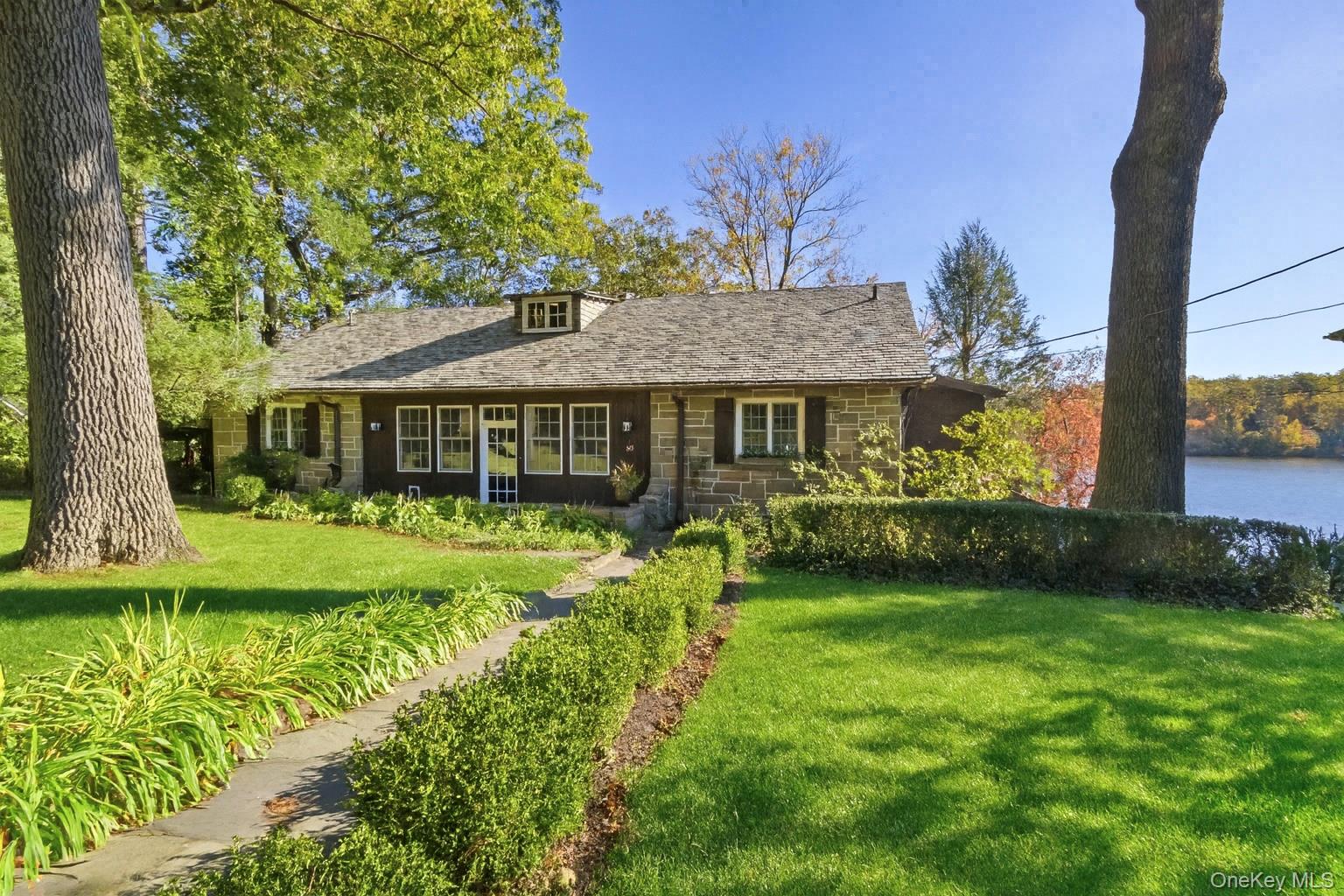 Set on the coveted waters of Lake Waccabuc, one of Northern Westchester’s most private and prestigious lakes, is a rare offering that blends architectural history with refined modern comfort. Originally crafted in 1939, the home was constructed of hand-cut Millstone granite and warm knotty pine paneling, a testament to old-world artistry and enduring character. The vaulted great room, with its floor-to-ceiling stone fireplace and original woodwork, pays homage to the home’s storied past. In contrast, the 2015 renovation introduced a striking, light-filled kitchen and dining area that opens to the lake through walls of glass. With custom cabinetry, a banquette dining nook, and seamless indoor-outdoor flow to multiple decks and balconies, this space perfectly balances history and contemporary design. The main level features a serene primary suite with private deck, spa bath, and dual walk-in closets, along with two additional bedrooms, including one with a cozy loft for extra sleeping space and a second full bath. The lower level offers a private office overlooking the lake and a guest suite with full bath and direct access to the water’s edge. A recently installed funicular provides easy access to the lakefront terrace, complete with outdoor fireplace, entertaining area, and expanded dock for swimming, kayaking, and boating. "The Bungalow" captures the spirit of Lake Waccabuc’s legacy and the ease of waterfront living today.