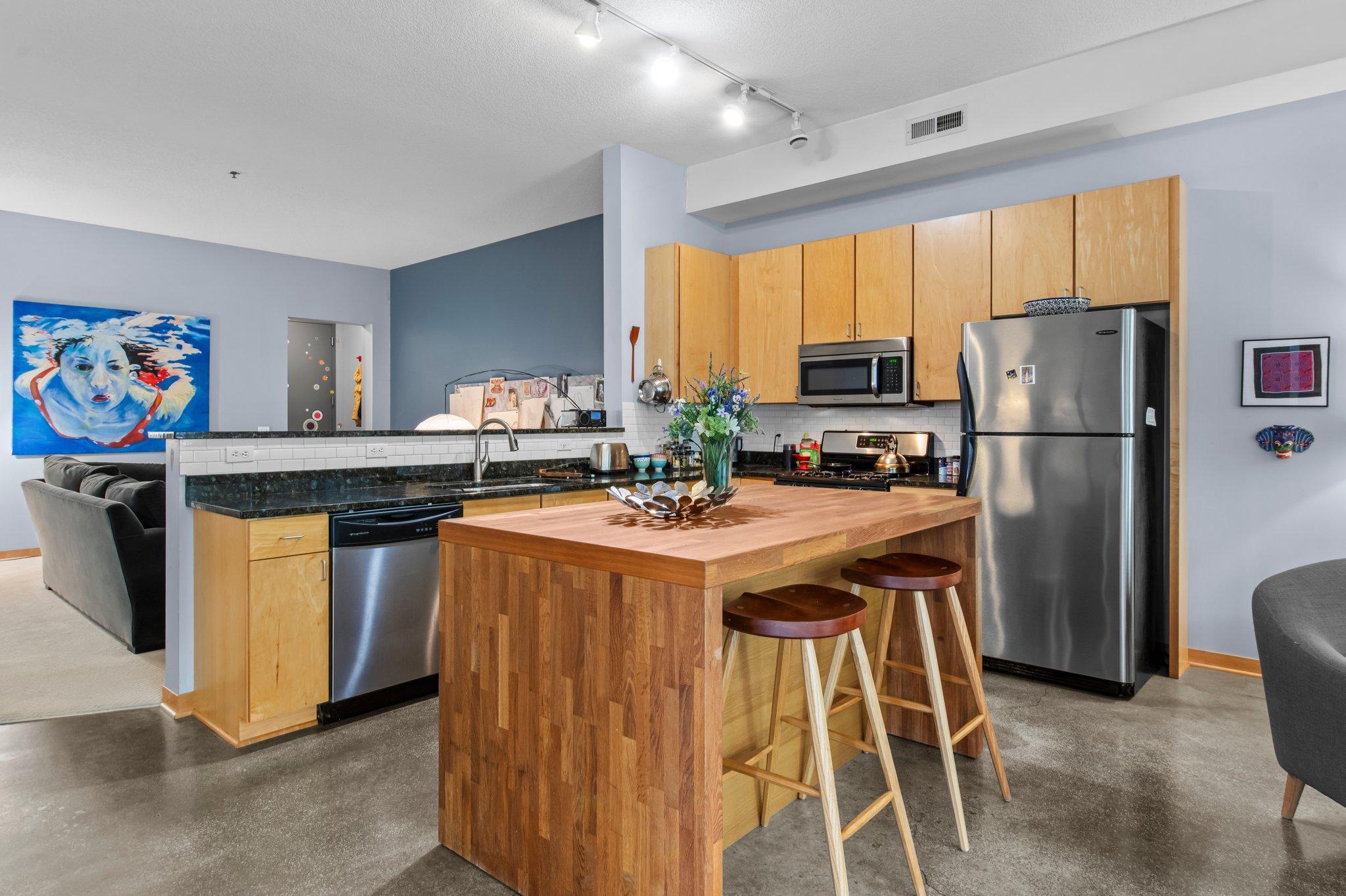 Ideally situated between Minneapolis and St. Paul, this one-of-a-kind residence offers the perfect blend of comfort, space, and urban convenience. Located just a few blocks off Highway 280 and steps from the Green Line Light Rail’s Westgate Station, commuting is effortless in any direction.
The building features a small grocery store right out front for everyday essentials—while this particular unit is located in the quiet rear of the building, well shielded from street noise for added privacy and tranquility.
Enjoy the close proximity to the Mississippi River and numerous surrounding parks, along with a wide variety of shops, cafes, and dining options, making the location both lively and practical.
Inside, the home stands out as the largest unit in the building—and the only one with this unique layout. This corner unit offers a rare blend of privacy, space, and natural light, beginning with a private street-level entrance and a welcoming 12x7 front porch, ideal for a morning coffee or evening unwind.
Step into the bright and expansive living area, where a floor-to-ceiling front window fills the space with sunlight. The 14-foot ceilings throughout add to the spacious, airy feel, making every room feel open and inviting. The living area flows seamlessly into a thoughtfully designed kitchen, complete with granite countertops, sleek stainless steel appliances, a stylish tile backsplash, and a center island with butcher block top and breakfast bar seating—perfect for casual meals or hosting guests. A nearby dining area adds more flexibility for meals or work space.
Tucked behind a frosted-glass barn door is the oversized 28x17 bedroom, a versatile and inviting space featuring multiple windows, allowing for abundant daylight. Whether used purely as a bedroom or as a combination sleeping, office, and creative space, it offers endless flexibility. A spacious 7x6 walk-in closet with built-in wire shelving ensures ample storage.
The full bathroom features updated tile flooring and a tub/shower combination, conveniently located near a hallway closet for linens and a stackable washer and dryer (new in 2025). Every detail is designed for function and ease.
Toward the rear of the unit, a cozy carpeted family room offers a quiet retreat—ideal for movie nights, a reading nook, or entertaining friends. An adjacent 8x7 walk-in closet provides even more storage, keeping the living spaces uncluttered and organized. A private rear door leads directly to the heated underground parking garage, where the unit boasts two assigned parking spots—a rare and incredibly convenient feature in this area.