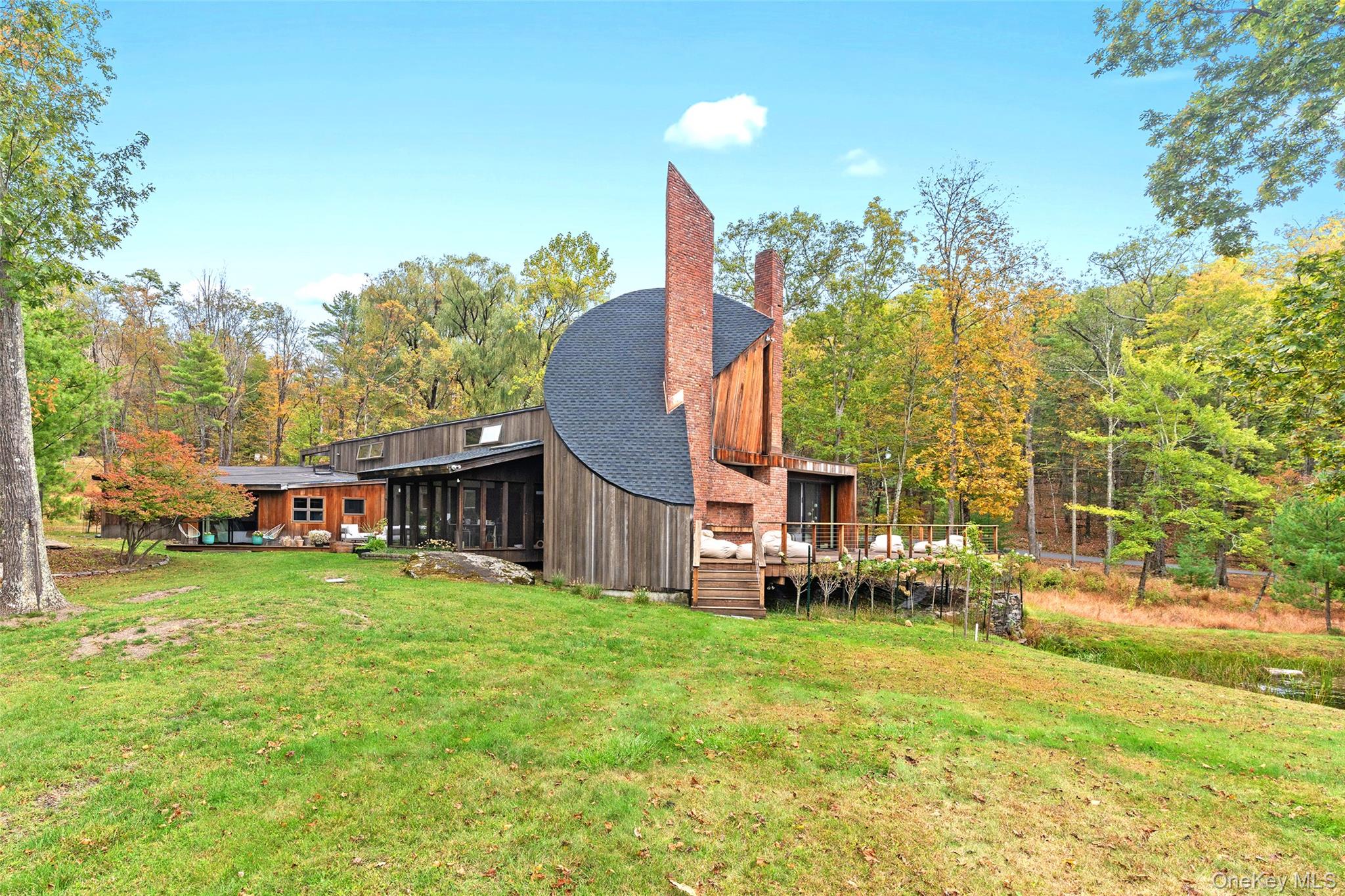 Set on nearly 9 serene acres in the heart of Woodstock's historic Byrdcliffe Arts Colony is a rare synthesis of architectural precision and natural harmony—an embodiment of award-winning architect John Storyk's deep understanding of space, sound, and site. Designed in 1969 at the very beginning of Storyk's now-legendary career—just after his groundbreaking work on Jimi Hendrix's Electric Lady Studios and the famous Bearsville Theatre—this redwood-clad contemporary home reflects his signature style: intuitive flow, warm natural materials, and an architect's sensitivity to both form and function. The 4 BR, 4 Bath, 4,000+ sq ft (includes guest/pool house) single family home is privately sited with a pond, heated in-ground salt water, gunite pool, and massive guest/pool house. This Mid-Century Modern sanctuary is defined by its soaring ceilings, custom mill work, and an organic relationship with the surrounding landscape. Every room is bathed in natural light through walls of glass, and oriented to maximize the surrounding views of meadow, woods, and sky. A dramatic curved, sunken living room—anchored by a large brick fireplace—evokes the sensorial immersion typical of Storyk's performance spaces. Here, spatial geometry and acoustics are not incidental but essential; offering not just a place to live, but a place to listen and feel. At the heart of the home is a Poggenpohl kitchen—a clean, functional workspace designed with the home chef in mind—that opens to dining and gathering areas which flow out effortlessly to the screened porch, expansive decks, landscaped gardens, and tranquil pond beyond; all designed to foster serenity and creative inspiration. Every line and threshold reflects Storyk's belief that architecture should support creativity and calm—never compete with it. Private spaces include a luxurious first floor primary suite and a guest apartment (with its own entrance) featuring a kitchen, full bath, and private deck—ideal for hosting, creating, or retreating. Across the entire property the interior volumes are balanced by exterior spaces with curated meadows, and reflective water elements including the large, heated, salt water, in-ground, Gunite pool) all reinforcing the idea of the house as an instrument tuned to its environment. While John Storyk is globally known for acoustically perfect studios and world-class performance venues, this home reveals another side of his genius: the quiet artistry of domestic space, where light, proportion, and stillness are as important as sound. A residence like this—designed by one of the 20th century's most innovative architectural minds, and located in a cultural enclave as storied as Byrdcliffe—is a truly singular offering. 289 Upper Byrdcliffe Road is not just a home, but a living, resonant experience—thoughtfully conceived, masterfully built, and deeply rooted in the creative spirit of Woodstock. Please note: Additional town-approved plans exist for a separate structure with its own septic and driveway entrance. All this coalesces to make an extraordinary compound with limitless options for a life well lived.