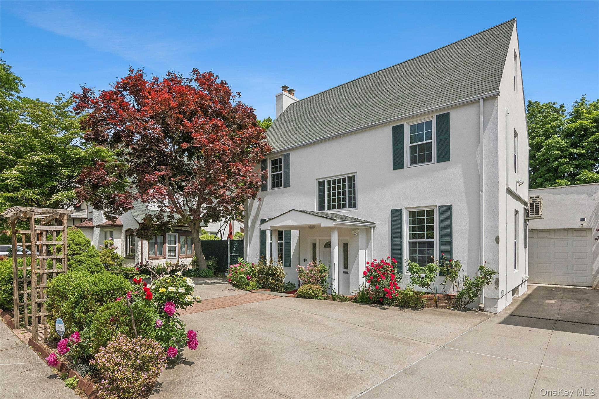 Nestled in the highly desirable Kew Forest section of Forest Hills, this beautiful stucco Center Hall Colonial blends timeless charm, elegant details, and generous living spaces throughout. Beautifully landscaped front gardens, a circular carport, a long private driveway, and an enormous detached garage create a warm and welcoming first impression.A charming entry vestibule leads to a gracious foyer and sun-filled formal living room centered around a wood-burning fireplace. French doors open to an expansive side patio, creating a lovely setting for relaxing outdoors or entertaining family and friends. The formal dining room flows seamlessly into a beautifully renovated open kitchen featuring quartz countertops, stainless steel appliances, abundant cabinetry and a door to the backyard. A convenient laundry room and half bath complete the main level.A sweeping windowed staircase serves as a stunning focal point, leading to the second floor where three generously sized bedrooms and a full hall bath await, including a spacious primary bedroom with an ensuite half bath. The third floor offers a private retreat with an additional bedroom, full bath, and versatile bonus room ideal for guests, a home office, or creative space.The finished basement provides an exceptional extension of the home’s living space, featuring a spacious tiled recreation room ideal for entertaining, relaxing, or creating a private retreat, along with a full bath, abundant storage, and convenient access to the back patio. Throughout the residence, rich hardwood floors and split-system air conditioning enhance the home's timeless elegance while providing modern comfort, creating a refined and welcoming atmosphere on every level.The expansive paved backyard offers ample space for outdoor dining, entertaining, and everyday enjoyment. A truly special feature, the enormous detached garage includes multiple storage rooms and a spiral staircase leading to a loft, offering endless possibilities for storage, a workshop, studio, or hobby space.Ideally located near the shops, restaurants, and cafés of Austin Street and Queens Boulevard, with convenient access to major transportation, this exceptional home offers the perfect combination of classic character, thoughtful updates, and comfortable living in one of Forest Hills' most sought-after neighborhoods.Some photos may be virtually staged