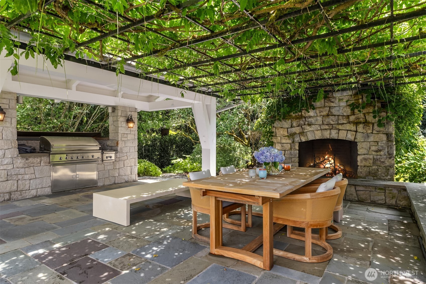 Covered outdoor living space featuring a stone fireplace and built-in grill.