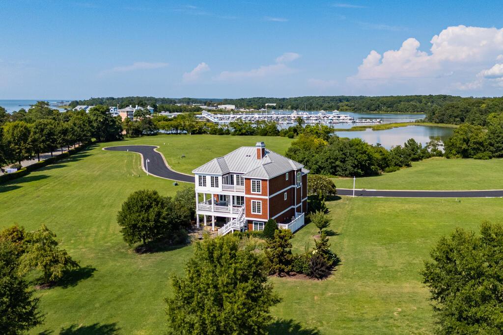 Gorgeous custom-built, cedar shake home in desirable Marina Village East, Bay Creek. Enjoy water views of the marina and Kings Creek, plus scenic views of the. lake from the back. Nestled on .28 landscaped acres, this beautiful home brings the outside in with lovely natural light through large windows and a well-designed layout. The property takes full advantage of its surroundings with thoughtful outdoor extensions, including a bluestone patio on the ground level tucked among gardens and specimen trees, two inviting covered porches, and a third-story deck! The lower-level 2-car garage boasts a fantastic finished workshop for the hobbyist in the family, a laundry room, and plenty of storage. An outdoor shower is located beside the garage, and tasteful fencing thoughtfully hides trash cans and outside HVAC units. Enter on the second level into a bright foyer with easy access to all connecting spaces. The welcoming living room, with its soaring 20-foot ceiling, centers the home and features a gas fireplace, built-in bookcases, and southern-exposure, two-story windows. Wrapping around the heart of the home, the main level features a kitchen with quartz countertops and a reverse-osmosis water filtration system, a pantry, a dining room, covered porches, a tall, bright study, a guest bathroom, and a guest bedroom currently styled as a den. The top third level features a wrap-around balcony peering over the living room. Off of this balcony, the primary ensuite enjoys a bonus open sitting room, access to a third-floor deck, and a walk-in closet. On the other side of the balcony, the additional guest ensuite bedroom accesses the same deck. An elevator, regularly serviced, connects all three levels. Perennial gardens designed by a local landscaper provide changing color, privacy, and inviting habitats for birds. Recent upgrades include a NEW HVAC system with sealed ducts installed in 2024, a NEW water softener installed in 2025, and a NEW third-floor deck and railings completed in 2026. NEW elevator inspection September 2026. New trim paint throughout the deck and porches, plus the manicured flower beds, highlight the extreme degree of care and maintenance this home has enjoyed since being built by the owners in 2007. Most furnishings convey, including the golf cart. A list of items the owner intends to keep will be available during showings. Non-membership required property.