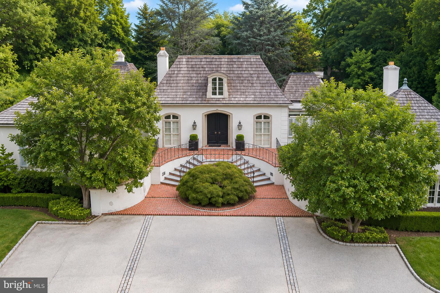 Exquisite 5,938-square-foot French Manor set on 3.54 acres of beautifully manicured grounds, which includes a 1.54 acre adjacent lot (Tax ID 40-00-58356-005) in the heart of Penn Valley is a must-see! Surrounded by mature landscaping, impressive stonework, and an in-ground pool, this exceptional residence offers gracious living spaces, timeless architectural details, and a wonderful connection to its spectacular, unique outdoor setting. Elegant crescent stairs lead to the main entrance and a sun-kissed foyer featuring marble tile and a soaring vaulted ceiling. The foyer opens to both the formal living and dining rooms, creating an ideal layout for entertaining. The impressive living room features beautiful hardwood floors, a cathedral ceiling, fireplace, and picturesque views of the backyard. Step up into the expansive formal dining room with rich wood floors and French doors opening directly to the rear patio. At the heart of the home is the gourmet chef's kitchen, thoughtfully designed with top-of-the-line appliances, a large center island with prep sink, abundant cabinetry, and generous workspace. The adjoining sun-filled breakfast room is surrounded by floor-to-ceiling windows and features built-in bench seating overlooking the grounds, along with two sets of French doors providing seamless access to the patio. The inviting family room offers exposed beams, a brick accent wall, fireplace, and beautiful views of the property. A wet bar and convenient powder room make this space perfect for both everyday living and entertaining. Privately positioned down the hall, the luxurious primary suite is a true retreat featuring its own fireplace, private access to the rear patio, a dressing area with custom built-ins and vanity, two walk-in closets, and two separate primary bathrooms. One offers a soaking tub and separate walk-in shower, while the second features a spacious walk-in shower. Two additional bedrooms, including one with a private en-suite bathroom, a full hall bathroom, and a conveniently located laundry room complete the main level. The lower level provides even more versatility with a spacious playroom or flex space, an additional bedroom, and a full bathroom with a sauna—an ideal arrangement for an au pair, guests, a home office, a gym, or extended living space. Ample storage and interior access to the 2-car garage complete this level. Outside, the property is truly special. Nearly two acres of beautifully landscaped grounds surround the home, highlighted by an in-ground swimming pool, extensive stonework, mature plantings, multiple patio areas, and a circular driveway. Ideally located within the award-winning Lower Merion School District, this exceptional Penn Valley residence offers a quick commute to Center City Philadelphia along with convenient access to major roadways, shopping, dining, and everything the Main Line has to offer. With grand entertaining spaces, flexible accommodations, resort-like grounds, and an exceptional setting, 243 Conshohocken State Road offers a rare combination of privacy, elegance, convenience, and timeless appeal.