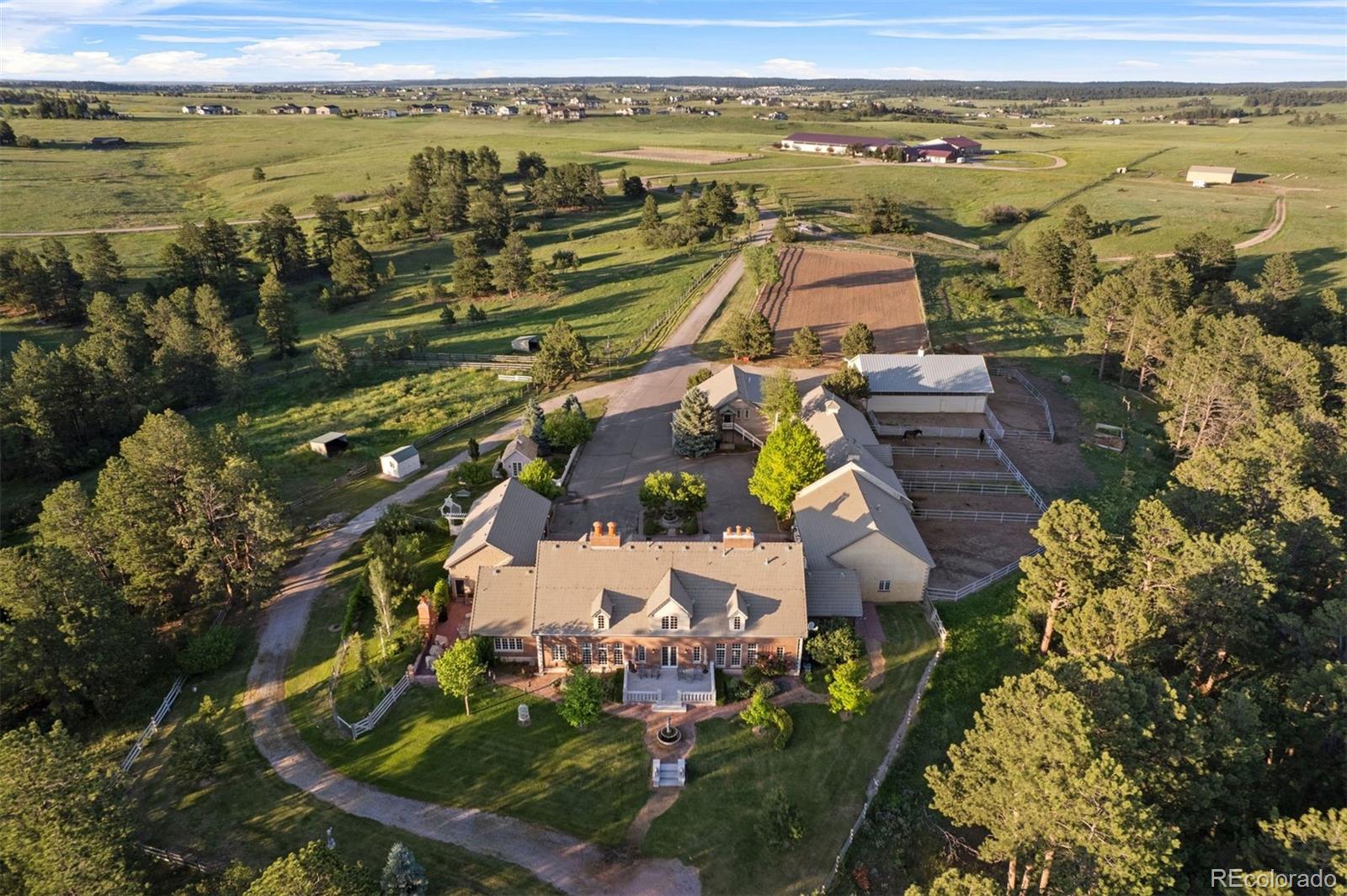 Immaculate and extraordinary, set on the most spectacular 80 acres in Douglas County! Trails wind through rolling terrain, open meadows, and wooded ravines, uniting into a breathtaking landscape. This pleasant, comfortable home is enhanced by the elegance of the architecture. A gated drive arrives at Thistle Hill Farm's circular courtyard and the stately residence with barns, a flex room, and garages on two sides. Under 15 minutes to Castle Rock and Parker. The entry hall is an architectural statement, passing through the home from east to west. 20-foot ceilings and a full wall of windows bathe refinished floors in the great room. The dining room seats 14 to 16 guests while retaining an intimate atmosphere. The kitchen features a butcher-block island and a hand-painted tile backsplash that adds warmth and artistry.  The private wing houses a serene primary suite, a study with custom fireplace, and a sunlit exercise room. Gallery access connects to the flex room, a distinctive space adaptable as a gym, studio, entertaining hall, or collection display area.  Outside, terraces and patios wrap every side of the home, an open invitation to enjoy the park that surrounds you. The west terrace highlights spectacular sunsets, while the kitchen patio with its fireplace, awning, and herb garden.With magnificent terrain and beautifully designed barns, Thistle Hill Farm is a horse property perfect for most disciplines. Indoor access leads to the heated stable with 7 stalls, a wash stall, 4 tie stalls, tack room, hay storage, and a full bath with laundry. A second barn adds 4 stalls, indoor round pen, and covered hay storage. The existing outdoor arena offers an ideal site for an indoor arena, with another location nearby perfectly suited for an outdoor arena. A 2-bedroom apartment offers flexible accommodations for guests or caretakers. Mineral and water rights included. An additional 40 to 120 acres of adjacent prairie grassland is available for purchase.