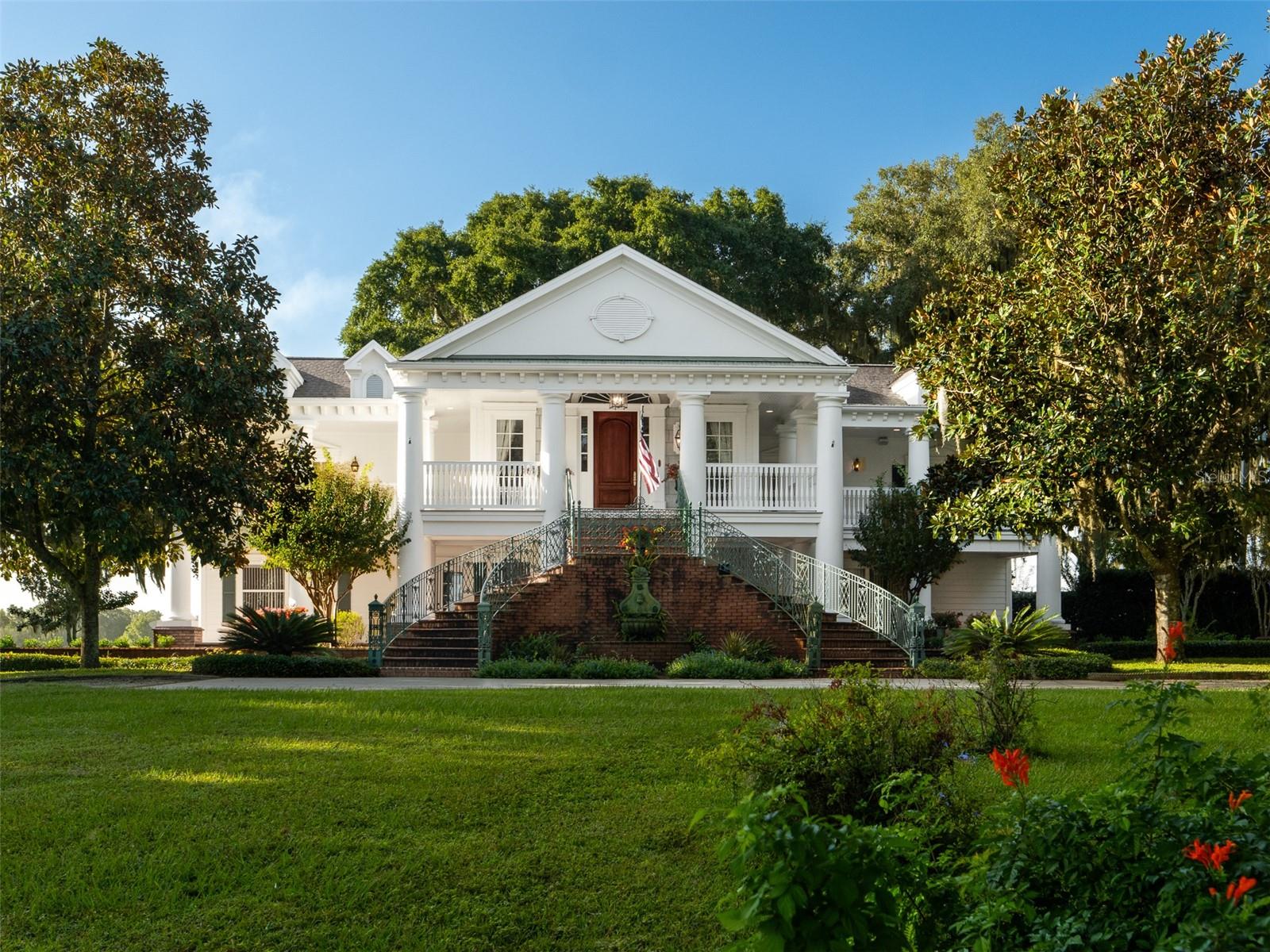 Located on 442+ acres, this remarkable property graced with elegant oak and magnolia trees offers expansive space, timeless Southern charm, and versatile living options. Ideally situated midway between Ocala and Gainesville, it’s just 8 minutes from the Jockey Club and approximately 25 minutes from the World Equestrian Center. A sense of peace washes over you as you drive through the open fields leading to the stunning two-story white Antebellum-style main residence, distinguished by its signature “welcoming arms” front entry. Inside, you’ll find 4 bedrooms, 4.5 baths, and 2 primary suites (one on each floor) with walk-in closets. The custom kitchen showcases wormy chestnut cabinetry and Carrera marble countertops. Rich cherry wood flooring flows throughout much of the home, complemented by tile and carpet in select areas. Expansive covered balconies span the upper level, with the back being completely screened, offering panoramic views of farm fields, woods, and wildlife, while matching brick patios extend below. An elevator ensures effortless movement between floors, and three fireplaces create inviting spaces throughout the home. The two-car garage with adjoining workshop adds practicality for everyday living and hobbies alike. The property also includes two additional residences, ideal for guest homes, family, or on-site staff. A true legacy estate offering privacy, beauty, and classic Southern elegance in a prime Central Florida location. Seller will consider subdividing.