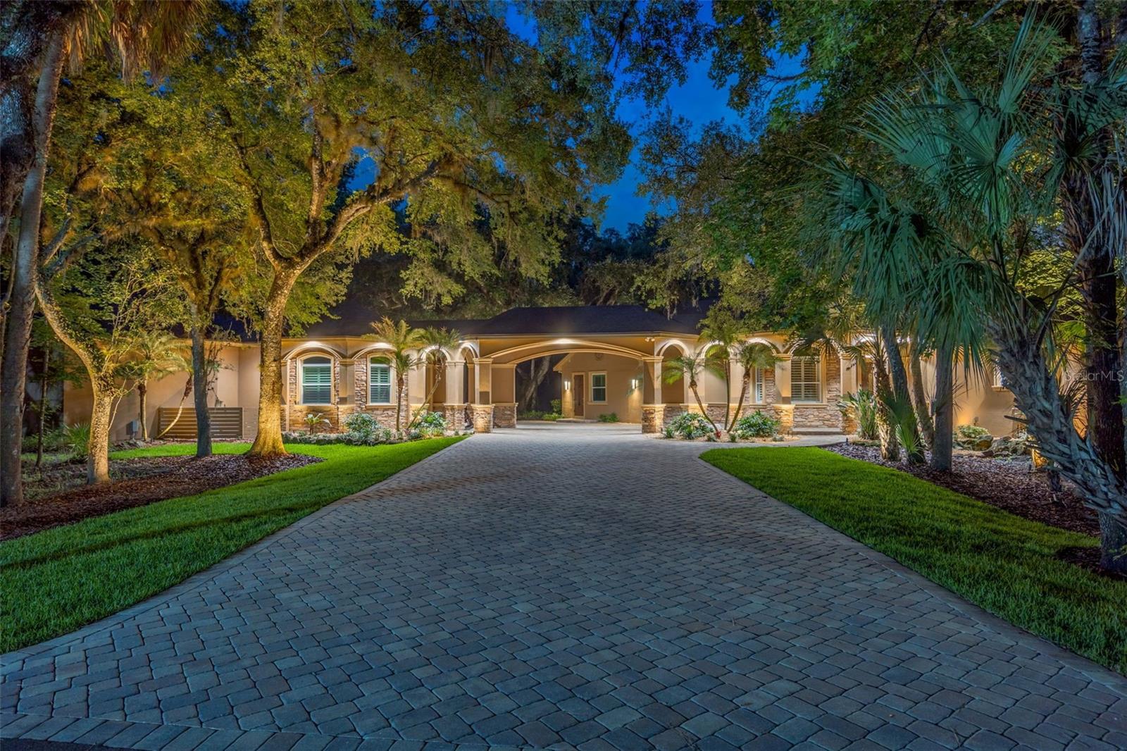 RARE OPPORTUNITY to live in The Estates of Riverpark in Tampa Palms, also a premier golf community!  This amazing estate is truly a one of a kind with over an acre of land, impressive privacy encompassed by woods and pond frontage, private iron gate entry, a spanning paver drive through a porte-cochere, guest house, outdoor fire pit, resort pool/spa, outdoor kitchen, and so much more perfect for entertaining!  You will enter the home via a wrap around porch as you step into a beautiful foyer with 12 foot ceilings and travertine tile.  You then spill into the sitting room or dining room whichever you prefer to make it with a beautiful concrete stained floor.  The kitchen is perfect for the family chef with stainless appliances, a top of the line Sub Zero, refrigerator drawers, a storage pantry with floor to ceiling cabinets, granite counters and an island sink.  The family room features an enormous space with a dry stack fireplace and triple sliders to open completely to the pool/lanai/outdoor kitchen-bar and additional outdoor casual space with yet another fireplace!  2 of the 6 bedrooms feature a Jack and Jill bath, tons of natural light and walk in built out closets.  The game room has cathedral ceilings and a gorgeous iron spindle staircase to elevate you to an additional private upstairs guest bedroom.  Your primary en suite boasts the most amazing custom built out his and hers closet, a beautiful free standing soaking tub and dual vanities.  The office is perfect for the at home executive. The guest house features a full bath and private entrance.  The 3 car garage truly can hold 4 vehicles and has a spacious stair accessible attic for outdoor storage!  Relax pool side overlooking the pond, dock, woods, and outdoor fire pit or dip into the hot tub or sit at the pool table with umbrella to escape the summer heat.  There is a shed that contains the pool equipment and ample additional storage with a refrigerator, freezer and shelving.  The home has a 10K watt solar panel system with a Tesla battery pack backup.  Come see this gem for it won't last long!