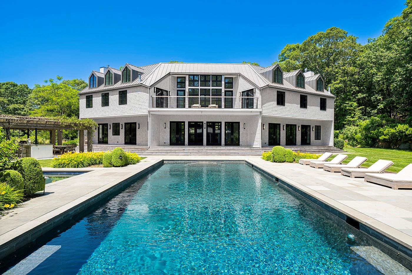 Modern Luxury in the Heart of Amagansett
Set on 2.44 acres of beautifully landscaped grounds, the home offers exceptional privacy and is ideally located across from South Fork Country Club-just moments from ocean beaches, shops, restaurants, and convenient transportation options. Spanning approximately 6,000 square feet across three levels, the home features 6 bedrooms, 7 full bathrooms, and 3 half baths. Light-filled interiors include multiple outdoor decks, a dramatic gallery space, and an open-concept kitchen and dining area with granite countertops and premium appliances by Viking, Miele, and Bosch. The main living room features a fireplace and adjacent office. The fully finished lower level offers an exceptional suite of amenities, including a gallery, home theater, wine room, game room, state-of-the-art gym, sauna, massage room (or optional sixth bedroom), and more. Outdoors, enjoy a luxurious lifestyle with a fully equipped kitchen for al fresco dining, a heated gunite saltwater pool with spa, pool house with fireplace, and a detached studio ideal for yoga, meditation, or fitness. Additional features include an all-weather tennis/basketball court, tennis shed, two outdoor showers, and an attached two-car garage. A rare opportunity in a prime Amagansett location-close to the South Fork Country Club, LIRR, the Jitney, local farmers market, and the vibrant village and beaches of Amagansett.