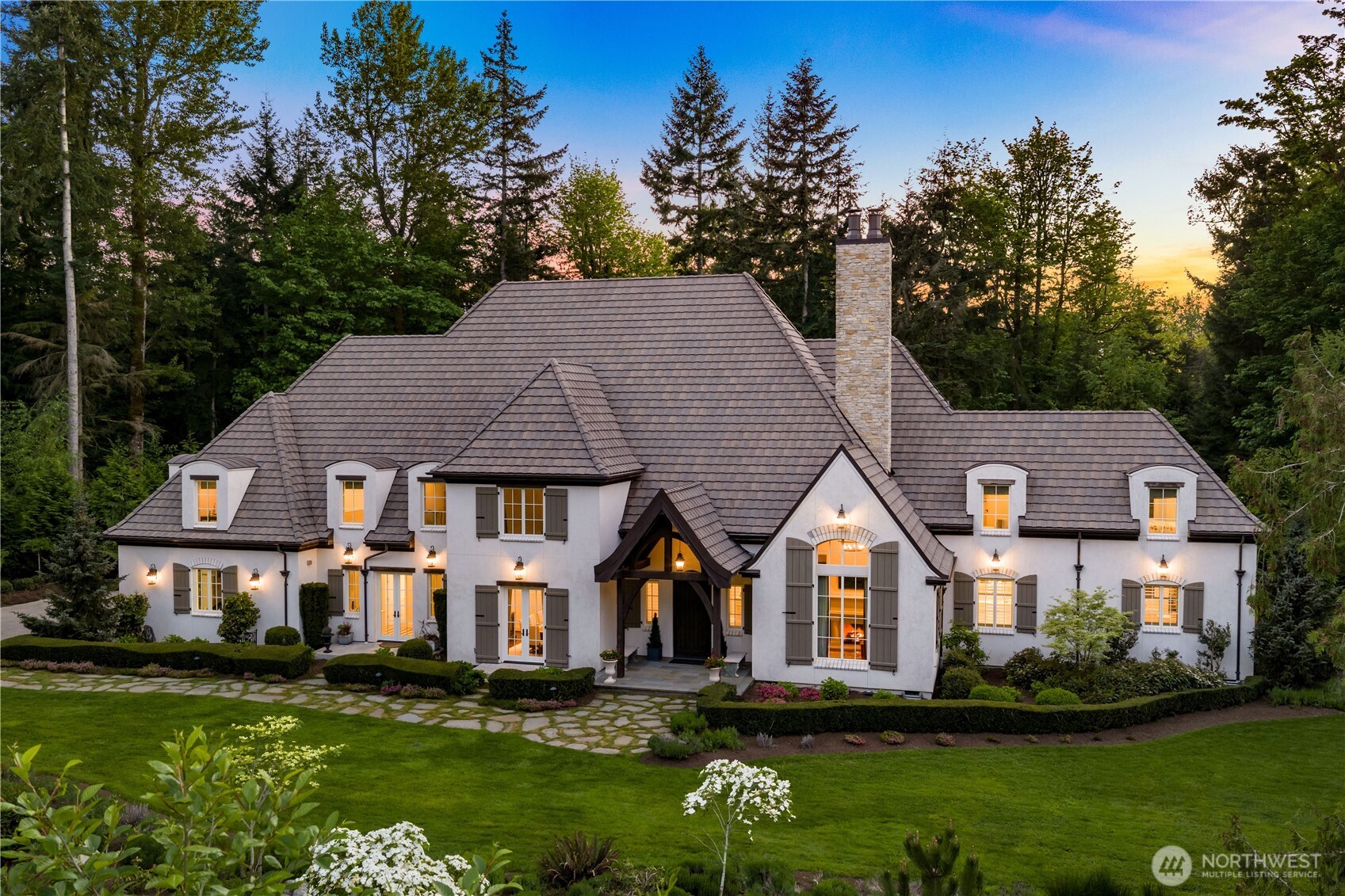 A rare confluence of French Norman elegance and modern luxury, this Grand Ridge estate commands 2.58 serene acres with an architectural presence that is immediately, unmistakably its own. Dramatic coffered and cathedral ceilings clad in rich walnut, a sculptural plaster range hood, herringbone hardwoods, and floor-to-ceiling windows overlooking protected woodland establish a standard of craftsmanship seldom encountered. The main-floor primary suite is a study in repose, with vaulted ceilings, a marble en-suite, and direct access to a private spa terrace with hot tub. Entertain in the formal dining room wrapped in wainscoting and candlelight, then gather in the grand room around a carved limestone fireplace before stepping outside to the covered stone terrace with roaring hearth and lush garden views dissolving into protected woodland. Every detail beyond the beautiful has been equally considered, from the systems that run quietly in the background to the spaces tucked away for creativity, entertainment, and rest. An estate of rare completeness.