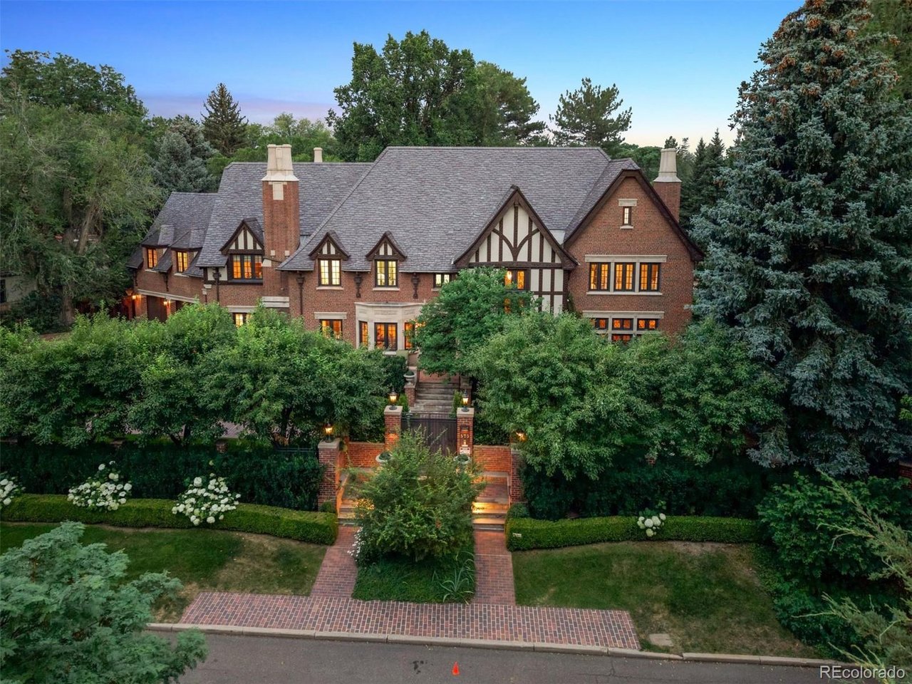 A rare opportunity to own one of Denver's iconic residences in prestigious and historic Denver Country Club neighborhood. Set on an exceptionally private, meticulously maintained 3/4+ acre lot, this remarkable property is surrounded by mature trees, lush landscaping and perennial gardens-an extraordinary setting just blocks from world-class shopping and dining of Cherry Creek North and minutes to Downtown Denver.Built in 1931 and designed by architect Henry Koch for Mason A. Lewis and Dorothy Fish Lewis, this brick and masonry Revival Tudor exemplifies timeless grandeur, thoughtful architecture and exceptional craftsmanship. Impeccable details throughout reflect a level of quality rarely recreated today, while extensive system updates provide the comforts of modern living.The main level welcomes with an elegant foyer, intimate living/reading room, and a grand salon anchored by a hand-detailed masonry gas fireplace, with design influences spanning Art Deco glamour, Moderne sophistication and traditional Period Revival artistry. A dramatic study/bar showcases custom built-ins and rich millwork. The formal dining room features luxurious wall coverings and lighting, while a butler's pantry leads to the bright kitchen and charming breakfast area with French doors opening to the spectacular backyard. Two designer powder rooms complete the level.Upstairs are five en-suite bedrooms, including a gracious primary retreat with private reading room, luxurious five-piece bath and generous closets. The third floor offers an additional en-suite bedroom, storage, and a rooftop patio overlooking the breathtaking grounds.The finished lower level features expansive entertaining space with gas fireplace, kitchenette, craft room, gym, sauna, massage room, 3/4 bath and wine cellar. A three-car garage and a custom-built temperature controlled wine cellar completes this extraordinary residence-a singular combination of architectural history, privacy and timeless Denver elegance.