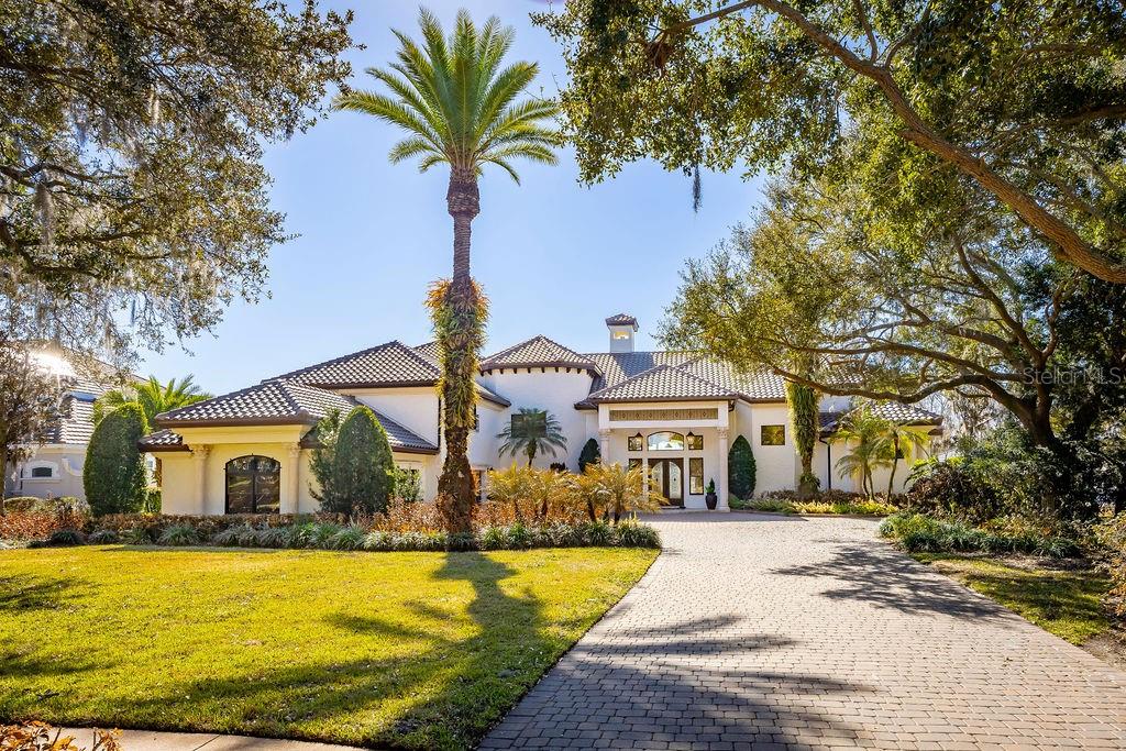 Extraordinary Lake Butler views abound from this classically elegant yet recently updated Chaine du Lac estate residence. Cradled in a private cove on Windermere’s signature lake on The Butler Chain, this showplace address stands supreme for its majestic presence, distinguished features and updates, and unsurpassed outdoor resort-style entertainment and living areas. Boasting a new roof, new reimagined primary retreat with a completely renovated bathroom and spa-like shower, new summer kitchen, refreshed game room/theater, and $100,000 designer lighting package by Lightstyle Orlando, this grand residence epitomizes glorious lakefront living. Inspired by tranquil golden sunsets, sparkling lake vistas, and elevated living, every detail has been crafted to create seamless living in a luxurious setting.  The sumptuous living and dining rooms are highlighted by soaring ceilings and a dramatic double-sided fireplace, while the spacious family room and breakfast nook seamlessly connect to the kitchen and open to serene water views. The primary suite is masterfully updated with modern appointments including beautiful vanities, an oversized walk-in shower, and a freestanding tub. The primary suite also features a gas fireplace and a private den, offering a quiet escape. A thoughtfully designed guest suite with its own sauna is also located on the main level.  Upstairs is a game room with full-bar, half bath, restaurant-grade smoke filtration system, and private balcony. A separate staircase leads to three ensuite bedrooms and newly unveiled recreation room with TV, table games, and built-in bar with beverage cooler. Across the pool deck is a flexible cabana space that can be used for a sixth bedroom, gym, or craft room. The outdoor living spaces are equally impressive, anchored by a spacious sundeck completely overhauled within the last few years that wraps around a shimmering pool accented by elegant fire pits. A newly updated summer kitchen sets the stage for effortless entertaining, while a grand pergola—complete with a loveseat swing and fireplace—offers a serene retreat. The property also features an immaculate sandy beachfront and a private double-slip boat dock keeping water toys within easy reach. A whole-home generator, 4-car garage, and high-energy HVAC units top the wish list of any home seeker. Experience the best of refined lakefront living in this iconic and move-in ready residence in one of Windermere’s most sought-after locations.