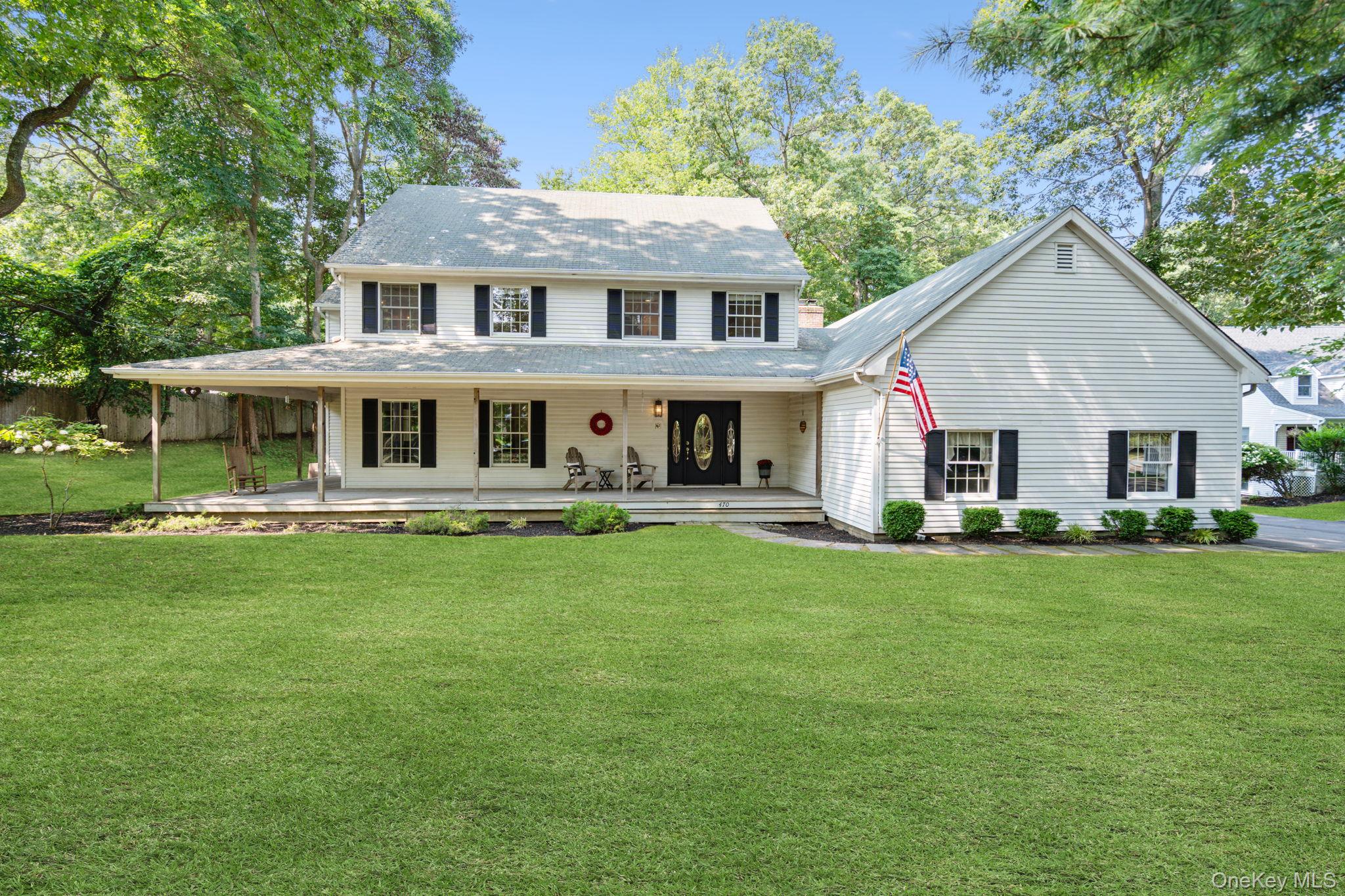 A spacious East Setauket home with a private road setting, wraparound porch, flexible office space, and plenty of room for everyday living. Set back on .56 acres, this American Farmhouse style Colonial offers approximately 3,000 square feet of living space, 4 bedrooms, 2.5 baths, and a flexible floor plan with a dedicated professional or home office area and its own side entrance. Built in 1990, the home features mahogany wood floors, tall ceilings, and a spacious kitchen with white cabinetry, a peninsula, and plenty of workspace. The adjoining den includes a fireplace and French doors that open to the rear deck overlooking a flat, partially wooded backyard. The separate side entrance to the office area adds flexibility for anyone looking for dedicated workspace at home without disrupting the main living areas. Additional features include central air conditioning, Andersen windows, two heating zones, two full stand up attics with separate access, a full basement with approximately 8 foot ceilings, a two car garage, and a Bosch washer and dryer less than five years old. Located in the Three Village Central School District with Nassakeag Elementary School, R.C. Murphy Junior High School, and Ward Melville High School. Convenient to schools, shopping, restaurants, Stony Brook University, Stony Brook Village, area hospitals, and major roadways.