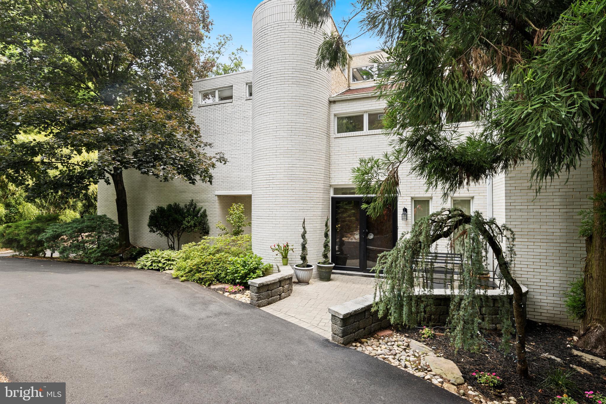 Tucked away at the end of a quiet cul-de-sac, this extraordinary custom contemporary residence offers a rare blend of architectural distinction and natural serenity. Thoughtfully designed to harmonize with its gently sloping 0.95-acre setting, the home is surrounded by mature landscaping, creating a truly private and tranquil retreat.A striking entry begins with elegant wood double doors, opening to imported marble tile that leads into the recently updated kitchen. Here, refined finishes meet modern functionality, featuring quartz countertops, a designer backsplash, ceramic tile flooring, and high-end stainless steel appliances. The open-concept layout flows effortlessly into a sun-filled breakfast area and inviting four-season room—ideal for everyday living and year-round enjoyment.At the heart of the home, the dramatic two-story great room impresses with soaring 30-foot ceilings and a full wall of windows that bathe the space in natural light. A wood-burning fireplace anchors the room, offering both warmth and visual appeal, while providing an ideal setting for relaxation or entertaining. A sculptural spiral staircase rises from the great room to a versatile lofted space, perfect for a private office, studio, or recreational area.The second level is highlighted by a spacious primary suite, complete with a luxurious bath, dual walk-in closets, and a private balcony overlooking the surrounding landscape. Four additional generously sized bedrooms and two well-appointed full baths provide comfortable accommodations for family and guests, while a large laundry room adds everyday convenience.The finished lower level expands the home’s living space with a second recreation area, bonus room, and full bath—well-suited for guests, extended living, or flexible use. Outdoors, a recently constructed 1,800-square-foot composite, multi-level deck and pavilion provide an exceptional setting for entertaining or enjoying the peaceful natural surroundings.Ideally located within the award-winning Lower Merion School District and just minutes from I-76, this distinctive home offers privacy, convenience, and timeless architectural appeal.
