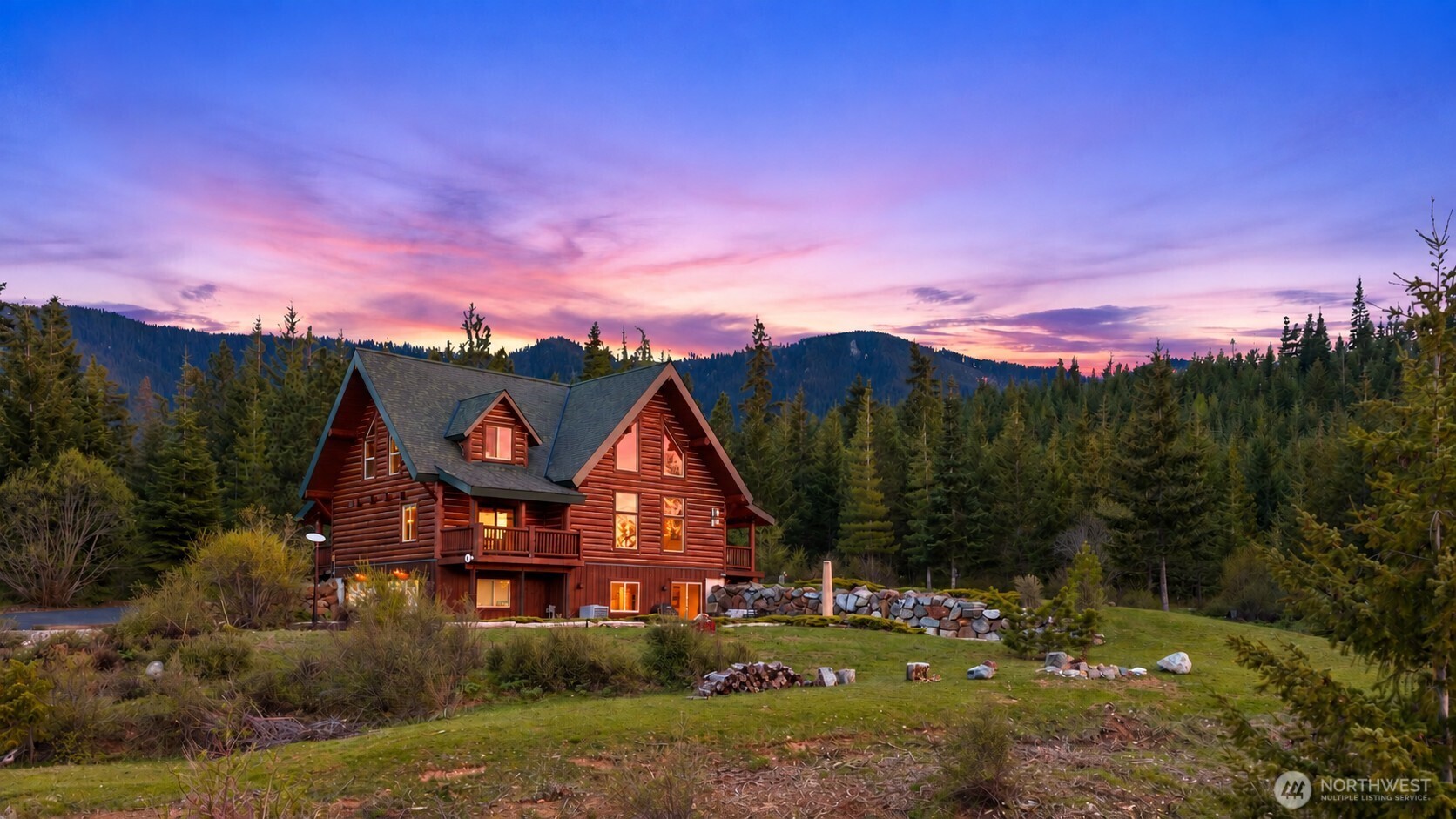 Twilight exterior showcasing the home’s warm log architecture and mountain backdrop.