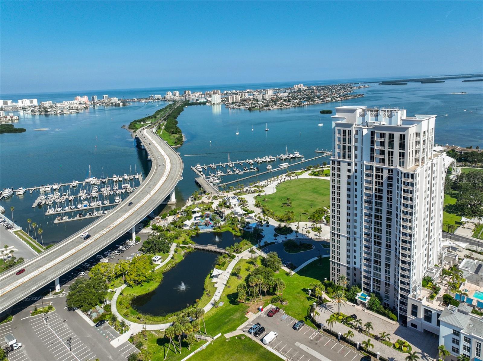 Enjoy stunning water and city views from this beautifully maintained 7th-floor condo at Water's Edge in downtown Clearwater. This spacious residence features an open living and dining layout with engineered hardwood floors and sliding glass doors leading from both the living area and primary suite to a private balcony overlooking the skyline. The kitchen is designed for both style and function with wood cabinetry, GRANITE countertops, tile backsplash, stainless steel appliances, and a large breakfast bar. A flexible den/office/bonus space adds versatility to the floor plan. The primary suite offers direct balcony access, a custom bath with dual sinks, and a large walk-in shower. The guest bedroom also enjoys water views and has an adjacent full bath and a  laundry room with stacked washer/dryer. Brand New AC replaced in January 2025. This unit also has TWO assigned GARAGE PARKING spaces and one storage space. Resort-style amenities elevate everyday living at Water's Edge. Residents enjoy a heated pool and spa with cabanas, outdoor grilling stations, and a cozy fireplace lounge overlooking the marina and Coachman Park. Indoors, you'll find a state-of-the-art fitness center with sauna, beautifully redecorated club and social rooms with catering kitchen and billiards, plus conference and event spaces ideal for entertaining. A 24/7 concierge provides security and convenience. Located in the heart of downtown Clearwater, you'll be just steps from the marina, Capitol Theatre, library, shopping, dining, and entertainment and only minutes over the bridge to Clearwater Beach. An easy commute to Tampa International and Clearwater Airports. Call today for your private showing!