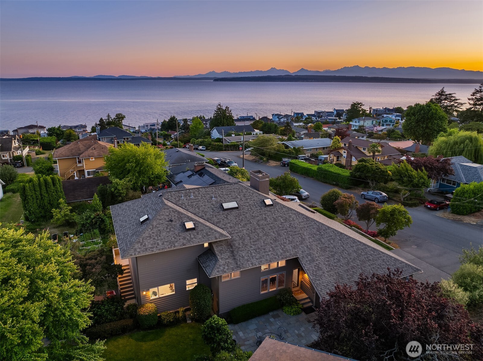 Nestled in coveted Richmond Beach, this architecturally distinctive Northwest Contemporary home captures sweeping Sound and Olympic Mountain views. A light-filled, three-level design showcases dramatic vaulted ceilings, skylights, and expansive walls of windows. The open-concept layout features thoughtfully placed cutouts that preserve airy sightlines while subtly defining each space. The chef’s kitchen is appointed with sleek black granite countertops, warm maple cabinetry, a generous island, and a built-in bench—perfect for casual dining or gathering. Directional gallery lighting enhances both the home’s architectural details and display spaces, while a modern two-sided fireplace adds style and warmth. Designed for flexibility and comfort, the ideal floor plan includes two bedrooms on the main level, three upstairs, plus a den, bonus room, and rec room. Step outside to an expansive wrap-around deck crafted from exotic wood, complete with a 20-foot Sunsetter awning, perfect for enjoying stunning sunsets. The primary suite offers a private view deck, walk-in closet, and spa-inspired bath. Additional highlights include professionally landscaped grounds with drip irrigation, integrated speakers and smart home features, a Tesla charger, and a new roof installed in 2022. Ideally located just moments from Kings Schools, parks, and the beach.