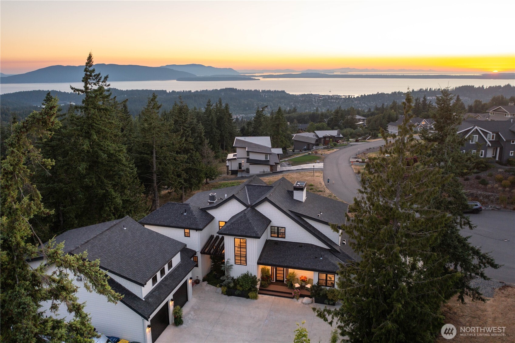 Perched above Bellingham with sweeping vistas of the San Juan Islands, Bellingham Bay, and beyond, this extraordinary residence blends architectural craftsmanship with modern PNW elegance. Designed to capture breathtaking views from every room, the home showcases a dramatic 28' vaulted fir ceiling & reclaimed beams salvaged from a historic Seattle pier. The main living area is anchored by an elegant 6' tile-surround gas fireplace w/ a honed granite hearth, while walls of glass open to the wraparound covered deck w/ 80' of west-facing frontage for sunset views & seamless indoor-outdoor living. The kitchen makes an immediate impression, with a generous quartz island, honed black granite countertops, and premium Thermador appliances. The main-level primary suite offers serene water views, a walk-in closet with Bosch washer/dryer, radiant floors, and a soaking tub. Upstairs, 3 bedrooms each feature a private en suite, along w/ a media room complete w/ a wet bar, bathroom, & private balcony. The main floor office, generous radiant-heated mudroom, finished 4 car garage, & additional parking enhance functionality. Motorized window treatments, whole-house AC, and generator provide year-round comfort and peace of mind. TimberTech decking, an 8-person hot tub, and extensive hardscape and landscaping complete the setting. Custom millwork, curated tile accents, and striking designer lighting elevate every space, creating timeless luxury in one of Bellingham’s most coveted settings.