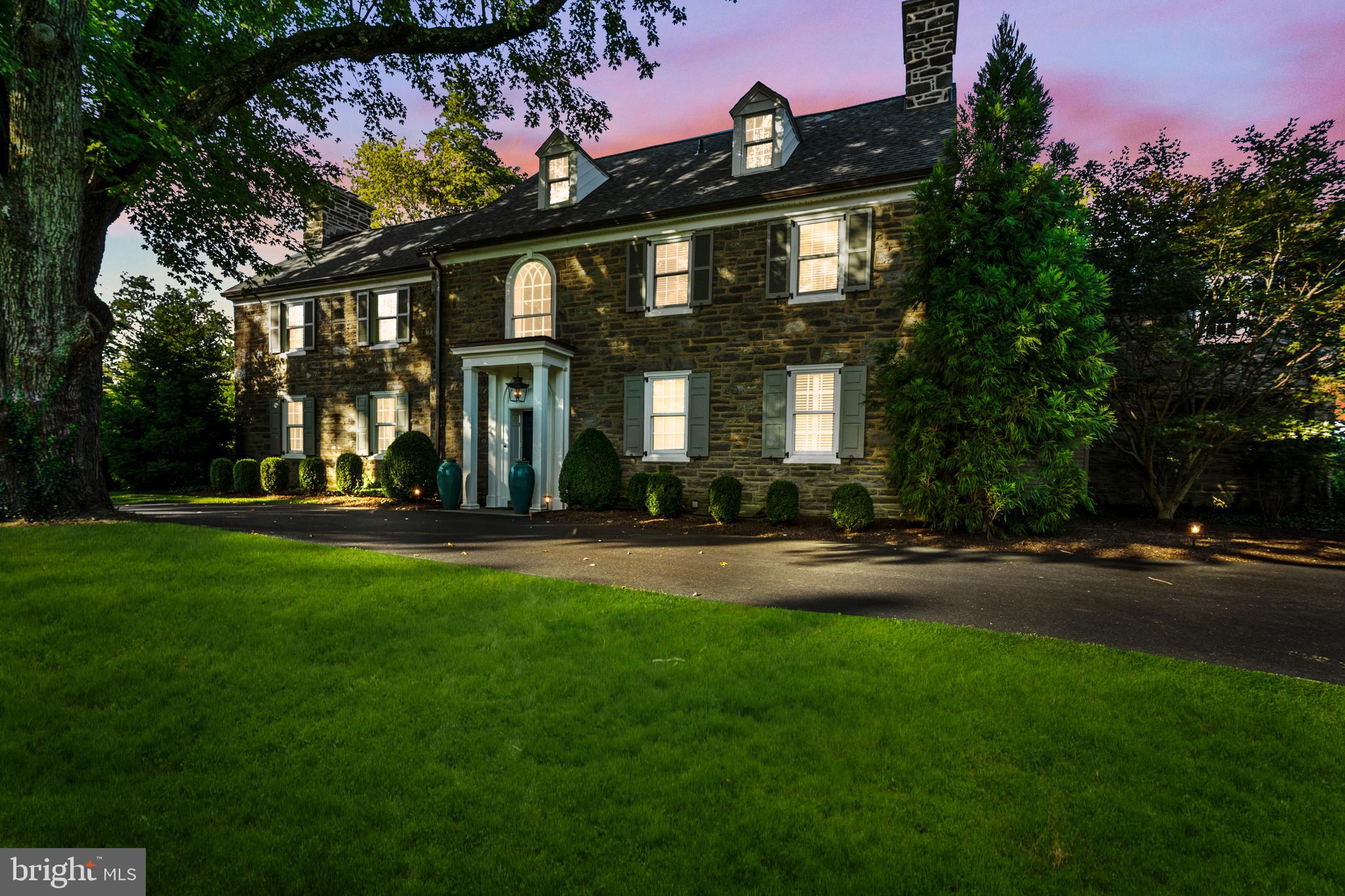 Classic and timeless, this Northside Haverford stone residence is gracefully sited on close to one acre of manicured grounds, where gardens, a shimmering pool, and tree-lined perimeters create a park-like setting. Approached by a circular drive that underscores its stately presence, the home reveals itself gradually balanced proportions, refined details, and interiors that have been thoughtfully modernized while honoring the architecture’s original spirit.A step-up center foyer introduces a striking axial view: through the dining room’s sweeping bay window with its intricate glass roof, the eye is drawn directly to the gardens and pool beyond. To the left, the formal living room offers an atmosphere of understated elegance. An oversized fireplace, flanked by tall south-facing windows, anchors the space, while richly stained hardwood floors, continuous throughout the main level, add warmth and cohesion. Another bay window provides symmetry when viewed from the rear, and French doors open to a covered stone terrace—an invitation to flow seamlessly between interior and exterior living.The kitchen is a study in contrast and comfort. Crisp white cabinetry plays against polished black stone countertops, while a substantial wood-topped island provides both prep and gathering space. A suite of Bosch appliances—including a steam/convection oven and dual dishwashers—makes the kitchen as functional for intimate dinners as it is for entertaining on a larger scale. Sunlight streams across the under-window sink, a small but significant detail that reinforces the room’s everyday ease.For moments of repose, the den offers a more intimate counterpoint: custom shelving, front-facing windows, and a brick fireplace create a retreat equally suited to reading or quiet evenings by the fire.Ascending the main staircase, an arched window becomes a focal point of architectural grace, as notable from the interior as it is when viewed from the façade. The primary suite, redesigned under current ownership, reflects both scale and serenity. The primary bath is anchored by a soaking tub positioned beneath a window, a spacious seated shower, and plenty of natural light from windows and large skylight.A newly created walk-in closet, complete with its own heating system, offers ample storage with a sense of luxury and care.Five additional bedrooms occupy the upper level—some connected by Jack-and-Jill baths, others with en-suite or adjoining arrangements—allowing flexibility and privacy. Anticipating the future, the attic has been spray-foam insulated, fully heated, and air-conditioned, ready for expansion should additional living space be desired.On the lower level, daylight streams into a casual gathering area with fireplace and deep window wells—an inviting setting for informal entertaining. A secondary staircase connects this space to the kitchen, leading also to a large laundry area, half bath, and generous storage.Outdoors, the home’s placement on its deep lot is deliberate and graceful. The covered terrace and poolside stonework blur the line between garden and architecture, while a recently re-roofed garden shed adds utility. A multi-car courtyard tucked to the rear offers discreet yet ample parking, underscoring the estate’s ability to welcome both intimate and grand occasions with equal ease.Classic and enduring, the home is one of balance and beauty—bright yet grounded, sophisticated yet welcoming—an estate of timeless appeal in one of Haverford’s most distinguished enclaves