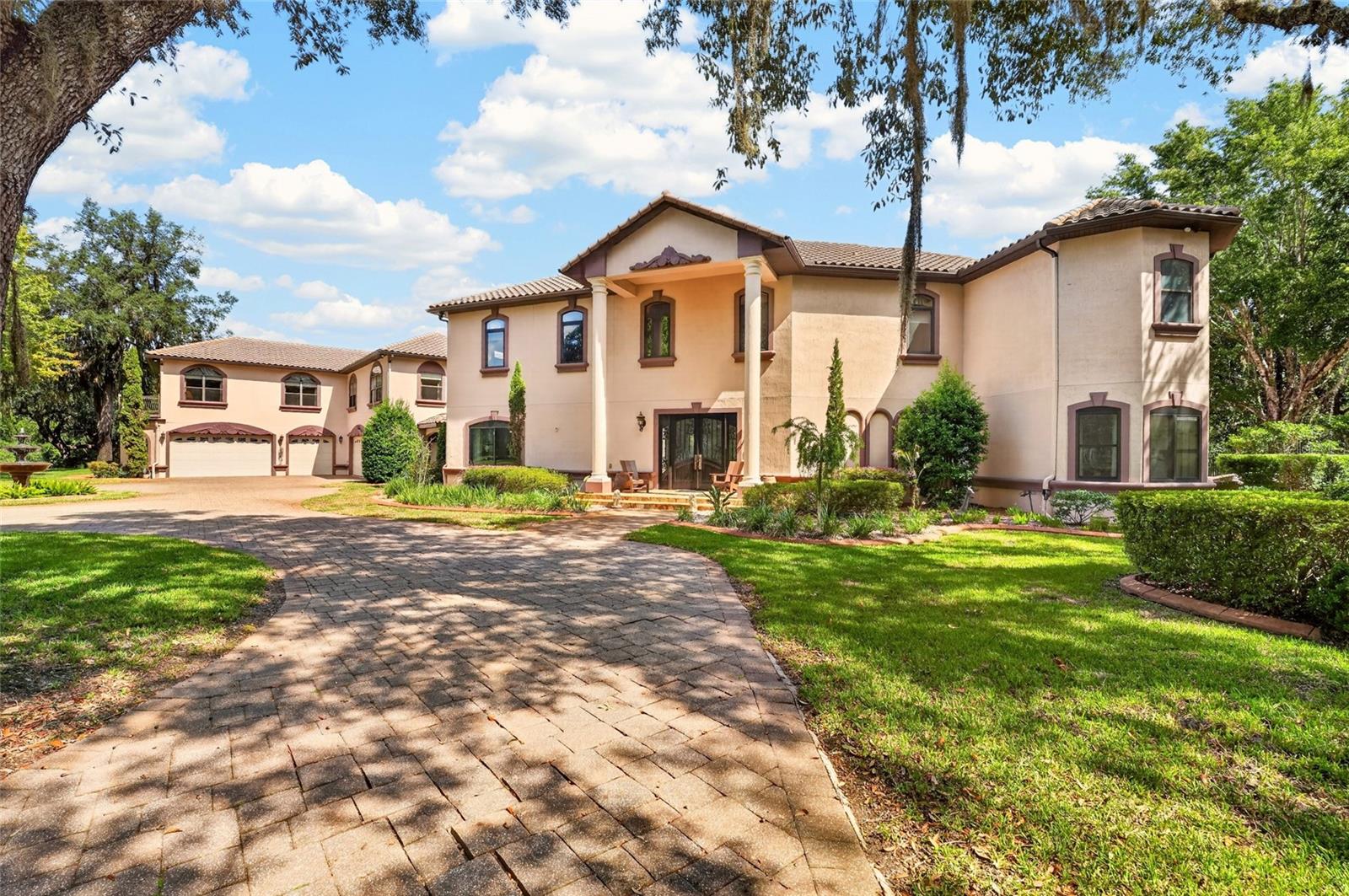 A remarkable lakefront estate unfolds across approximately 14.07 acres with 318 feet of frontage on 44-acre, spring-fed Hardesty Lake, combining waterfront access, expansive acreage and substantial residential and recreational space. This distinctive Interlachen property encompasses two parcels and features a two-story main residence, pool and spa, covered boat dock and private boat ramp, a detached six-car garage with a two-bedroom apartment and an additional two-car aluminum barn. Approximately 6.84 acres contain the residence, garage and barn, while 7.23 acres are cleared, undeveloped land. Built in 2008, the two-story main residence offers approximately 4,506 square feet under heat and air with four bedrooms and three baths. The first floor opens with a vaulted foyer, marble flooring and a distinctive staircase and upper walkway. The living and family rooms are connected by a double-sided fireplace, while the family room features travertine flooring and a custom bar. The kitchen, living room and dining room capture views of the pool and lake. The kitchen features a large granite island, granite countertops, custom cabinetry, two sinks, two disposals and gas cooking. An adjacent kitchenette and walk-in wine room with a cooling system and custom door complete the space. Additional details include 10-foot ceilings, crown molding, marble windowsills and baseboards, designer doors and chandeliers. Upstairs, the primary suite features a fireplace, wet bar with mini refrigerator, built-in walk-in closet and access to a screened balcony. The marble primary bath includes a walk-in double shower, two sinks with granite countertops, a jetted tub and separate vanity area. A den/office with built-in shelving and French doors also opens to the balcony. Two additional upstairs bedrooms share a Jack-and-Jill bath, with one providing balcony access and views of the pool and lake. Outdoor living centers around the pool with a multilevel stone waterfall, additional water features and spa, complemented by the fenced backyard, pool storage room, upper deck and exterior spiral staircase connecting to the pool deck. A circular paver driveway with a fountain garden leads to the residence, while a lighted main gate marks the property entrance. A covered walkway connects the main residence to the detached two-story garage. The garage provides six-car capacity with space to accommodate a 27-foot boat, automatic garage doors, drive-through capability, a half bath and dry sauna. Above, approximately 2,200 square feet of conditioned living space includes two bedrooms, two baths and an open kitchen, dining and living area. The apartment features quartz countertops and island, a gas fireplace, front and rear upper decks and elevated views across the lake and property. Additional property features include a 24-by-26-foot aluminum two-car barn, two wells, two septic systems, central vacuum systems, propane tankless water heaters, a 10-zone irrigation system, security features and whole-house generator wiring. The property is located outside town limits and has no homeowners association. Call to schedule your opportunity to view this one-of-a-kind estate today!