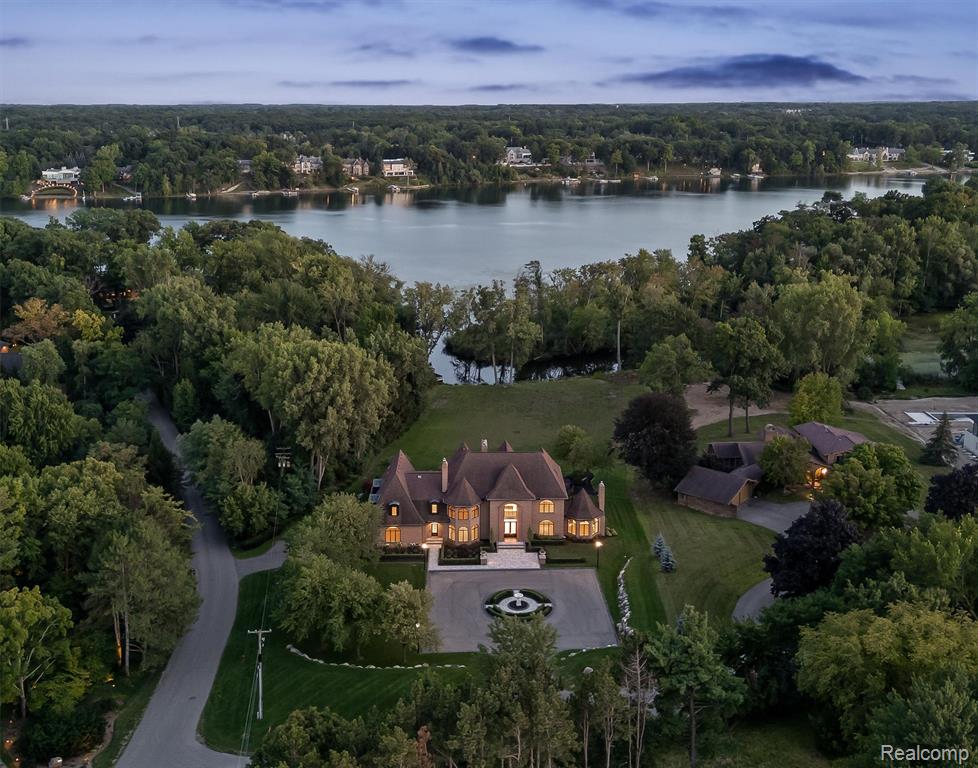 Set on over two acres along the coveted shores of all-sports Upper Straits Lake and directly across from Orchard Lake Country Club, this estate offers the rare combination of newer-construction quality, timeless design, and resort-style amenities. A grand foyer with Cinderella staircase opens to interiors of exceptional scale, with formal living and dining rooms, a fireside family room, and multiple sitting areas for both entertaining and everyday living. The chef’s kitchen impresses with dual built-in refrigerators, custom cabinetry, stone surfaces, oversized island, and Miele coffee station, flowing seamlessly to the breakfast room and expansive deck with panoramic lake views. The second-floor primary suite is a private retreat featuring sweeping lake vistas, sitting room with fireplace and wet bar, spa-inspired bath, and private laundry. Additional bedrooms across the second and third floors provide flexible accommodations, including a convenient first-floor ensuite. The walkout lower level offers the ultimate in recreation with a fireside great room, game room, spa with sauna and showers, and an incredible year-round indoor pool with jacuzzi. Outdoors, enjoy manicured grounds, brick paver terrace, maintenance-free decking, and private dock access to Upper Straits. Additional features include two elevators, central vacuum, surround sound, and full smart home integration. This property blends the presence of a grand estate with the benefits of newer construction in one of Oakland County’s most prestigious lakefront settings. B.A.T.V.A.I