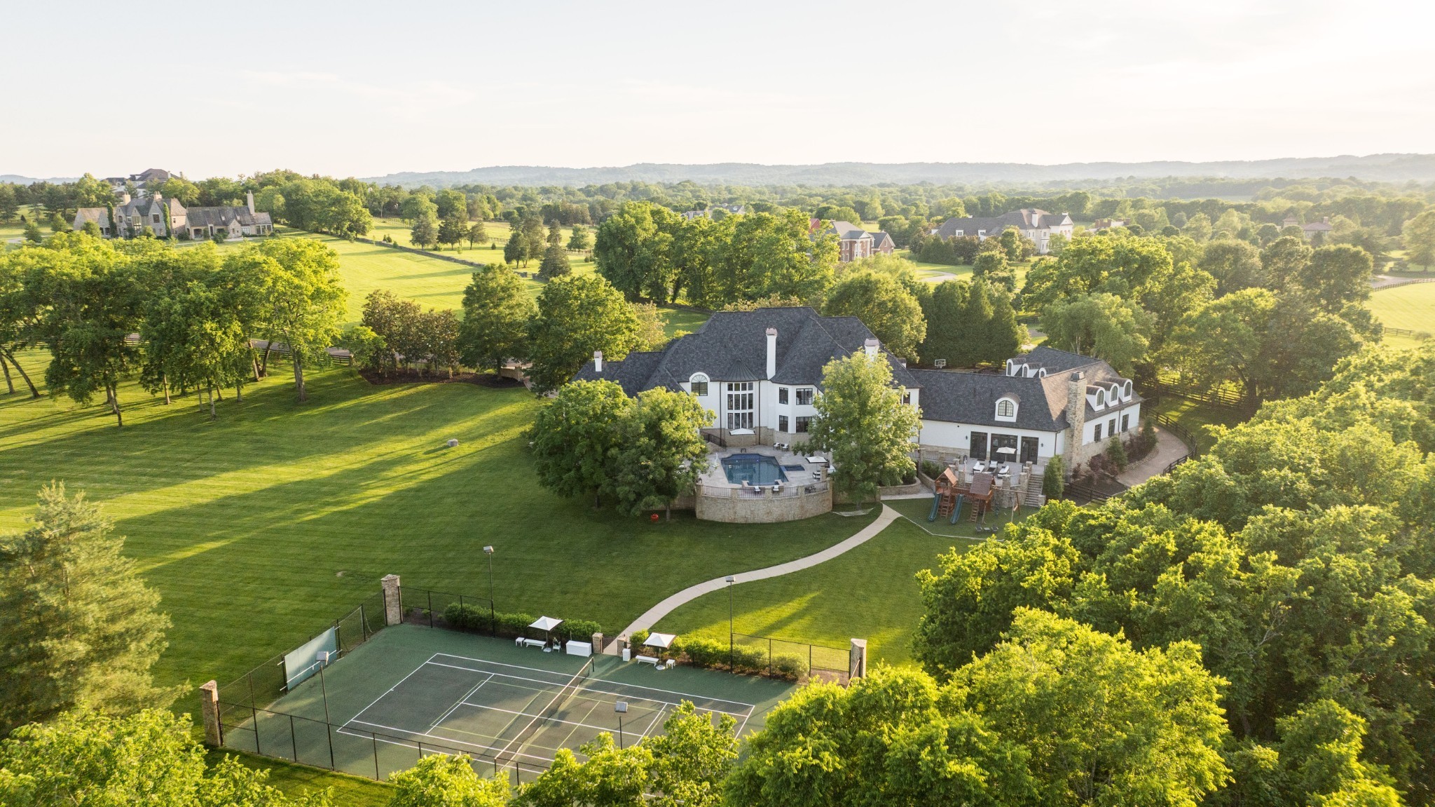 Tucked within one of Franklin’s most exclusive gated communities, 2410 Hidden River Lane is the epitome of modern Southern elegance. Set on nearly six private, level acres with flat green pastures and direct access to scenic community horse trails, this estate offers the rare balance of quiet luxury and purposeful design—just minutes from the charm of downtown Franklin and the vibrancy of Nashville. Completely reimagined since 2022, the residence features over 15,000sqft, 5 bedrooms, 9/3 baths, a newly constructed chef’s kitchen adorned with marble countertops, custom cabinetry, and a full wet bar with wine cellar for effortless entertaining. The interior is graced with wide-plank white oak flooring, curated designer lighting, and an elegant marble foyer that sets the tone for the rest of the home. The primary suite offers a serene escape with a spa-inspired bath, dual vanities, soaking tub, and an expansive custom dressing room. Additional enhancements include a private sauna, a state-of-the-art home theater with new projector and seating, and whole-home smart automation system. Guest quarters include an additional 2,000 sqft of living space. Outdoors, the transformation is equally stunning. A newly resurfaced and tiled pool anchors the backyard, flanked by an extended patio, updated gas firepit, and a fully renovated exterior bar that services a dedicated pool bath—ideal for seamless indoor-outdoor living. The grounds are meticulously maintained and professionally groomed, with manicured turf play areas, a full-size sport court, and a charming children’s playground. Custom pathways wind through blooming hydrangeas, cherry blossoms, magnolia trees, and vibrant maple plantings. With a new roof and copper gutters, updated security and surveillance systems, and an advanced water filtration system, no detail has been overlooked. 2410 Hidden River is more than a home—it is a private estate crafted for those who appreciate elevated design and natural beauty.