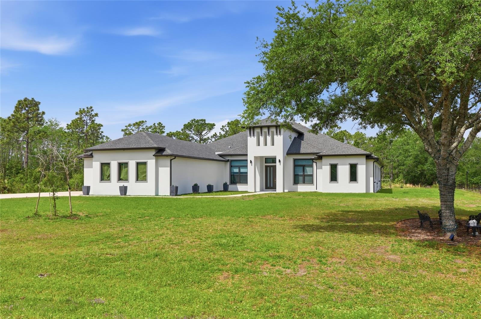 Some homes check the boxes, but this one raises the bar! This custom-built luxury home in Orlando’s Wedgefield community offers 4 bedrooms, 3 bathrooms, a three-car garage, and 3,417 square feet of living space on a 1.24-acre lot. Move-in ready with a level of detail that is evident the moment you arrive. Once you step into the foyer, the home immediately makes a lasting impression. Straight ahead, the space opens into the main living area, where soaring ceilings, an open layout, and natural light fill the home. Marble-look porcelain tile runs throughout, while a custom painted acrylic accent wall anchors the living room as a striking focal point. Coffered ceilings, crown molding, and statement chandeliers bring a polished, elevated finish. To the right of the foyer, a private office with French doors offers a quiet, well-placed space to work or focus. Also on this side of the home, the primary suite is set apart, designed with handicap accessibility and delivering every indulgence, including a freestanding soaking tub, a glass-enclosed walk-in shower, dual vanities, a private water closet, and a room-sized walk-in closet that serves as its own private dressing room. Moving into the main living area, the kitchen and living spaces connect with ease. The kitchen features quartz countertops, soft close solid wood 42 inch cabinetry, a large island with seating and plenty of storage, along with a walk-in pantry. The laundry room is conveniently located nearby, complete with cabinetry, shelving, and a sink. The dining area sits just beyond, well positioned for both everyday meals and entertaining. From the living room, oversized multi-panel sliding glass doors open to a covered back porch, extending the living space outdoors. The porch offers plenty of room for a future outdoor kitchen, gatherings, or a screened-in retreat. To the left side of the home, the guest wing is thoughtfully laid out. Two bedrooms share a Jack and Jill bath, while the third bedroom is positioned near a separate guest bath, with the hallway providing direct access to the back porch. The property has been leveled with fill dirt and is ready for what comes next. Whether you envision an accessory dwelling unit, additional parking, or future expansion, the groundwork is already in place, including a dedicated electrical panel ready for future connection. Added insulation over the garage and porch helps keep the home comfortable and energy efficient year round, and a whole house filtration system is in place. This home has an unbeatable location in the highly sought-after Wedgefield community, offering easy access to SR 528, 417, Orlando International Airport, and top-rated schools. Schedule your private tour today because this is the one!