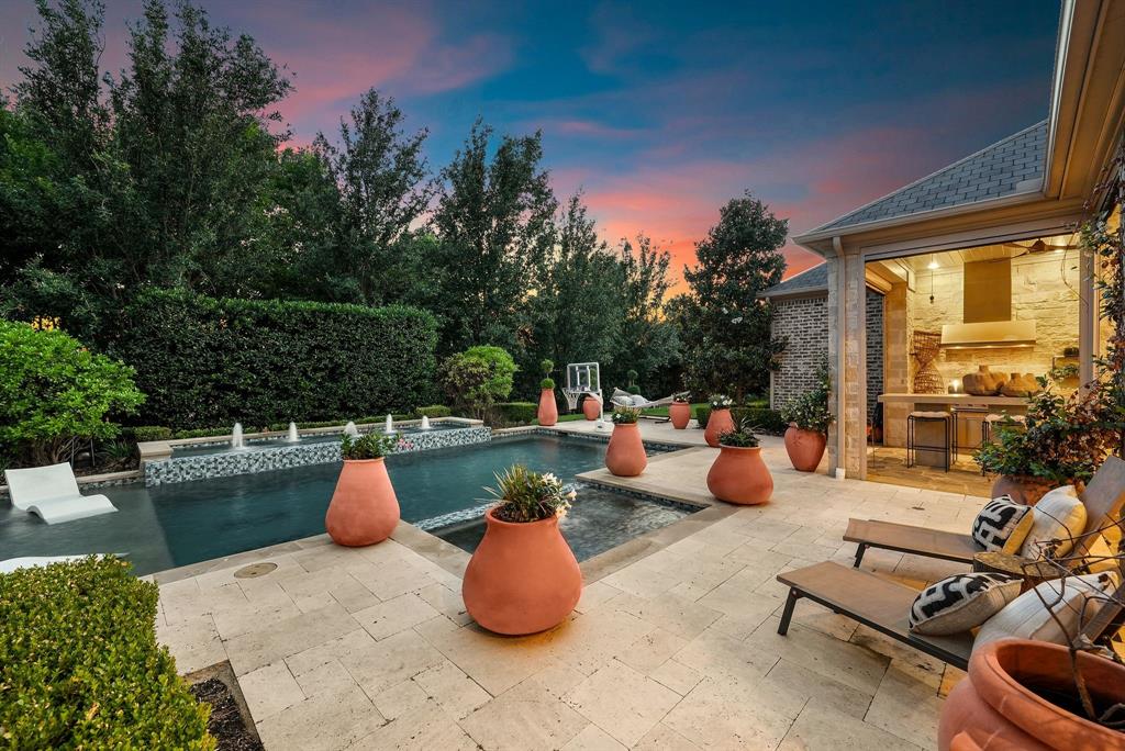 Located on nearly half an acre within the prestigious guard-gated community of Normandy Estates, this custom Greg Alford home offers one of the most sought-after floor plans in today's luxury market. Designed for both everyday living and entertaining, the 1.5-story layout features three ensuite bedrooms on the main level, a private study, formal dining room, versatile bonus room, upstairs guest suite with dedicated media room, and a built-in storm shelter for added peace of mind. Just minutes from Legacy West, The Star, and both DFW International and Love Field airports, the location offers the perfect balance of privacy and convenience. Designed to embrace indoor and outdoor living, the backyard is a private retreat featuring a heated pool and spa, fully equipped outdoor kitchen, expansive covered patio, motorized screens, mature landscaping, and exceptional privacy, creating an ideal space for entertaining or relaxing year-round. Inside, timeless craftsmanship is evident throughout with hand-scraped white oak flooring, soaring wood-beamed ceilings, designer lighting, a cast limestone fireplace, and oversized windows that fill the home with natural light. The chef's kitchen is thoughtfully designed with an oversized quartz island, custom illuminated cabinetry, a 7-burner gas range, double ovens, dual dishwashers, wine refrigerator, and abundant prep space. Rarely does a home combine a highly desirable floor plan, resort-style outdoor living, exceptional craftsmanship, and a premier guard-gated location in one of West Plano's most sought-after communities.