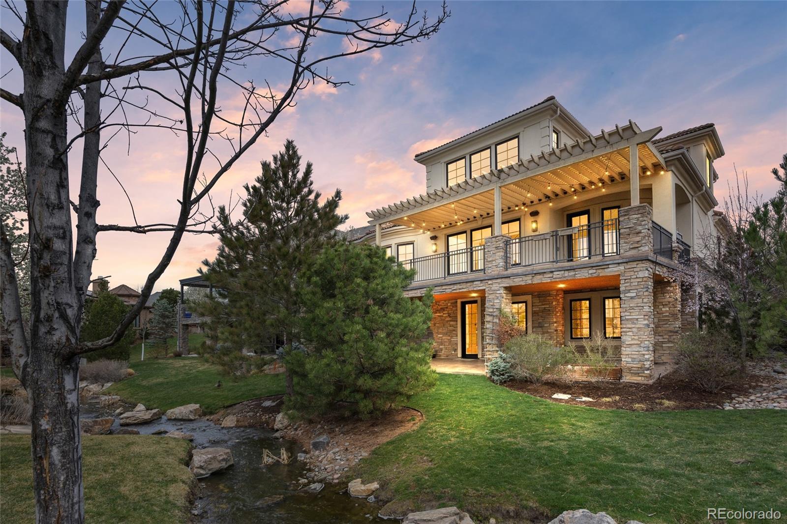 Exceptional custom home perfectly positioned on a quiet interior street within one of Denver’s premier golf communities, this residence offers a blend of elegance and serenity. Designed for seamless indoor-outdoor living, the expansive deck with multiple seating areas and custom pergola provide an inviting setting for entertaining or simply unwinding. Inside, a thoughtfully designed open floor plan is both functional and refined. The chef’s kitchen is truly impressive with its professional-grade appliances, ample cabinets, pantry, oversized island with storage and bar seating and a sunny breakfast nook. Host the holidays with ease in the formal dining room--complete with a custom table and two banquette benches accommodating up to 12 guests—and an inviting living room with gas fireplace and 2-story ceiling with windows overlooking the back deck. A main-floor study offers a private work-from-home retreat large enough for 2. The main floor primary suite is a luxurious sanctuary, filled with natural light and complemented by a spa-inspired bath with dual/split vanities, soaking tub, oversized shower with dual heads, linen cupboards, and walk-in closet with organizational system. A large laundry room and half-bath complete the main level. Two spacious en-suite bedrooms upstairs are joined by a versatile loft. The finished walkout basement further elevates the home, offering a private living space with two bedrooms, two bathrooms, a generous recreation area, and wet bar. The covered patio opens directly to the lawn and stream, enhancing the home’s connection to its serene setting. A large unfinished area provides ample storage or the opportunity for future customization. Two HVAC systems and two hot water heaters enhance the comfort of this home. With its walkout basement, stunning water views, and thoughtfully curated living spaces, this home offers a lifestyle defined by comfort, sophistication, and effortless Colorado living.