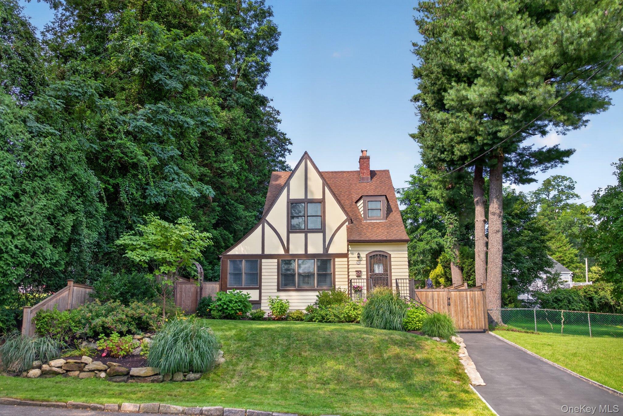 Tudor-style home situated in the highly desirable Poet’s Corner neighborhood—a fully updated, turn-key jewel inside and out. Step into a welcoming foyer, which flows seamlessly into a sun-filled living room anchored by a wood-burning fireplace and elegant custom built-ins. Glass pocket doors open to a serene, four-season sunroom ideal for a dedicated home office or reading nook.At the heart of the home, the open-concept kitchen and dining area sparkles with modern finishes and features sliding glass doors that lead directly to the private outdoor retreat. Upstairs, you will find a bright primary bedroom with dual closet space, a second bedroom with fitted storage, and a beautifully appointed full hall bathroom.The recently finished lower level expands your living space with a second full bathroom, a cozy family room, and a wet bar complemented by custom built-ins and ample storage—offering fantastic guest room potential. Step outside to your lovely sanctuary, complete with professionally landscaped perennial flower beds, an automated sprinkler system, and a 6-foot cedar privacy fence enclosing the backyard. The local Bee-line bus stop at the end of the street offers easy access to the Metro North Train station with express trains to NYC. Close proximity to major shopping, restaurants, parks and wonderful recreational facilities.