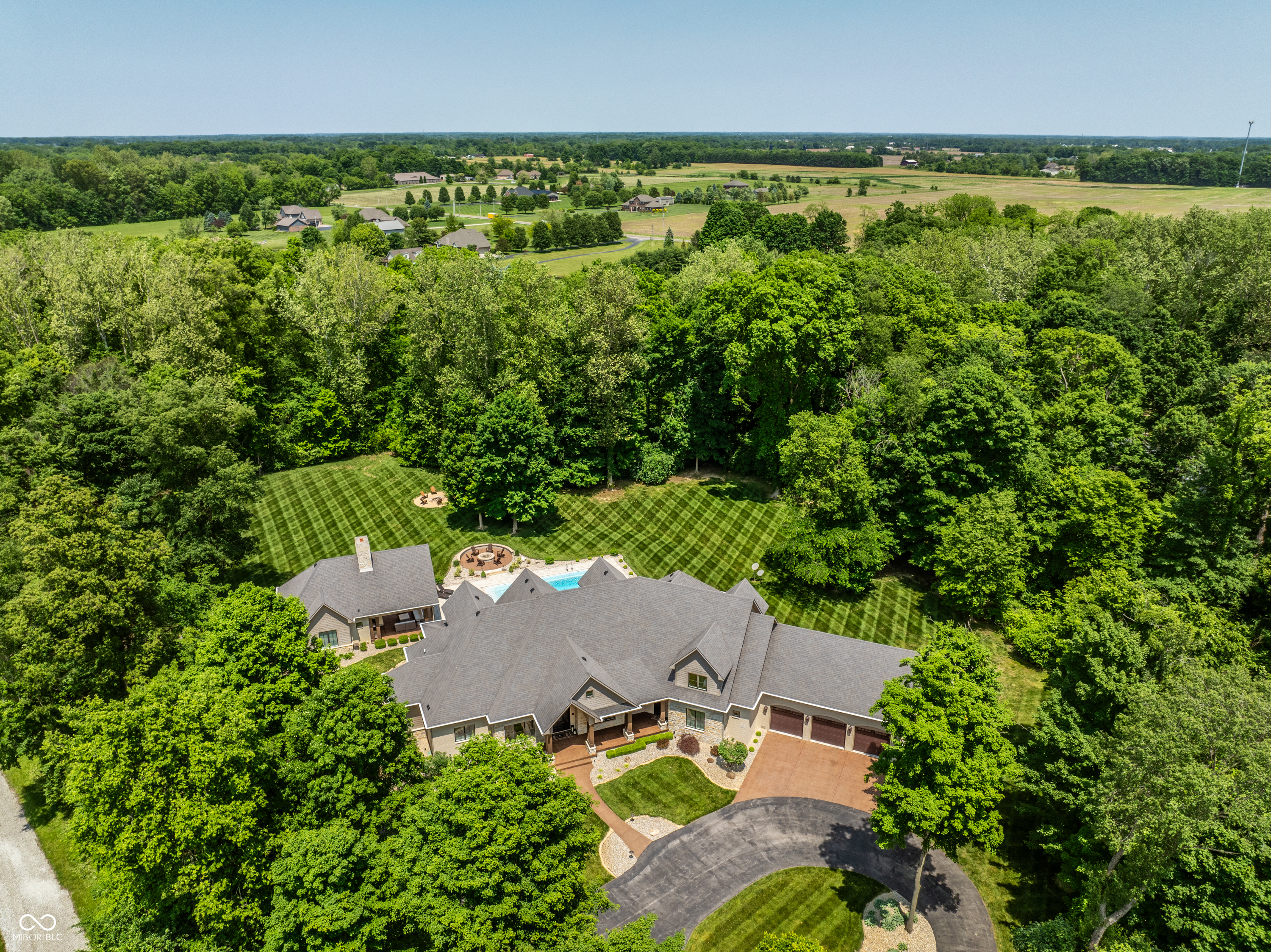 Nestled behind a private stone entry gate on 5 wooded, meticulously landscaped acres, this custom estate built by Mike Duke Custom Builder in 2016 offers refined living with every detail thoughtfully designed. Featuring 4 bedrooms, 4.5 baths, and over 5,700 square feet of high-end finishes, this home blends timeless craftsmanship with modern comfort. The main level showcases an open-concept layout with 10' ceilings and 8' doors, a soaring beamed cathedral ceiling in the great room and seamless access to a full-length covered porch from the kitchen, sunroom, and primary suite. The gourmet kitchen is a chef's dream-Thermador appliances, a 10-foot island with seating for six, granite counters, butler's pantry with private catering entry, and a temperature-controlled 750-bottle wine cellar. The main floor primary suite offers a spa-inspired retreat with a 2023-renovated En-suite bath, walk-in shower, soaking tub, and a spacious closet with its own washer/dryer. A separate main floor in-law suite includes a private bath, walk-in closet, and rough-ins for a kitchenette. Upstairs you'll find two additional en-suite bedrooms, a media/rec room, and office. A finished workout room with walkout access to a fenced patio, formal dining room, and an executive office with custom cabinetry round out the main living spaces. Step outside to a true backyard oasis: a 20x40 Gunite pool with diving board, automatic cover, and paver surround; hot tub; outdoor pavilion with stone fireplace, kitchen, gas grill, sink, refrigerator, and Green Egg; plus gas and wood-burning fire pits. A detached 2-car garage with half bath, epoxy floors, adds even more flexibility. Additional features include: 3-car attached garage with dog wash, slat wall, and storage. Anderson 400 series windows and sliders. Generator, dehumidifier, reverse osmosis system, Invisible fence, Control4 audio system, alarm and video surveillance. 3 HVAC units, and much more.