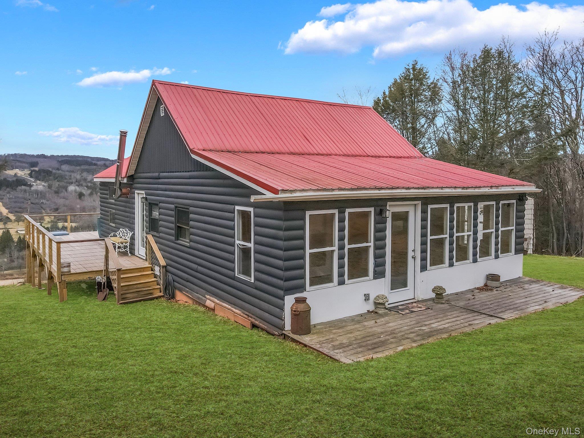 Front of house with metal roof, a yard, and a wooden deck, and expansive vista in the background