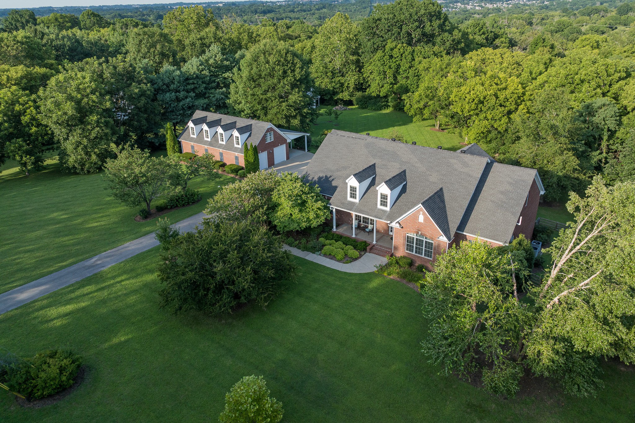 Set on five private, wooded acres, this all-brick property delivers space on a different scale: almost 9,000sf of heated & cooled living space, 2 main-level bedroom suites, a walk-out basement; and beyond the home, an outbuilding/workshop with power adds another 3,300 square feet under roof for hobbies, cars, equipment and storage.Inside, a vaulted great room rises around a floor-to-ceiling stone fireplace and skylights, while living and dining rooms add coffered and tray ceilings. The kitchen includes granite counters, a 6-burner gas cooktop, double ovens, warming drawer, pot filler and 48-inch built-in refrigerator. The primary suite provides built-ins, a walk-in closet and bath with steam shower, garden tub and double vanities. A second main-level suite adds flexibility; upstairs are 2 more bedrooms with private baths, a rec room and a theatre room with refreshment area.Then there is the basement—3,438 square feet that changes how this home can live. Seven windows and French doors add natural light, and the layout includes 2 large living areas, a kitchenette without a range, an office, full and half baths, flex/work areas and generous storage. A separate exterior entrance opens to a covered lower patio beneath the upper porch.The full-brick detached building was designed to complement the home, but its utility is the real story. Three overhead doors, an air-conditioned workshop, 120/240V power, work sink, cabinetry, half bath, epoxy-coated floors and a fully decked upper level create serious capability for projects, collections and storage. A tall-clearance carport expands the covered space for recreational equipment or oversized vehicles.Established trees, landscaping, gardens and covered outdoor spaces complete the setting. With no HOA and convenient access to Nolensville, Brentwood, Nashville, nearby parks & shopping and I-24, this south Davidson County property combines privacy, flexibility and an amount of usable space that is difficult to duplicate.