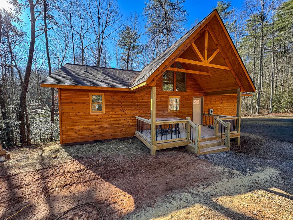 Brand New Construction Cabin in the Hiwassee Dam Community Welcome to this beautifully crafted new construction cabin tucked into the peaceful Hiwassee Dam community. Thoughtfully designed with a 2 bedroom, 2 bath split floor plan, this home offers privacy, comfort, and timeless mountain style. The heart of the home is the inviting great room, featuring open wood beams and a stone-framed wood-burning fireplace, creating a warm and welcoming atmosphere. The spacious kitchen is outfitted with custom cabinetry, ample workspace, and flows seamlessly into the living area—perfect for entertaining or quiet evenings at home. Throughout the cabin you'll find hickory luxury vinyl flooring, excellent closet space, and a roomy laundry room complete with a laundry sink. The primary bath showcases a tiled walk-in shower with quality finishes. Enjoy outdoor living from covered front and back porches, plus open decking off both bedrooms overlooking a private, wooded backyard—ideal for relaxing, morning coffee, or unwinding at the end of the day. A circle driveway provides easy access and convenient entry from the main road. Whether you're looking for a full-time residence, mountain getaway, or low-maintenance investment, this brand-new cabin delivers comfort, privacy, and quality craftsmanship in a desirable location.