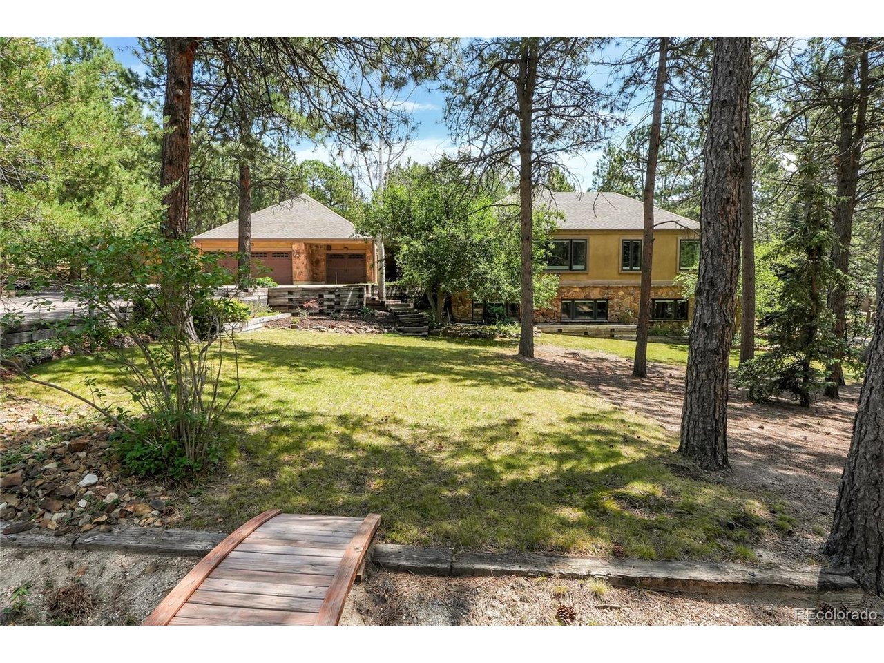 This is the home you've been waiting for! Located in the sought-after Woodmoor community, this spectacular custom home offers the perfect blend of timeless character and thoughtful updates, with the opportunity to add your own personal style. Large sized rooms throughout provide exceptional space for both everyday living and entertaining. The home features four fireplaces, four bedrooms, including a main-level primary suite, and a basement bedroom suite too, a gourmet kitchen, two living rooms, two family rooms, a library, an office, a spacious main level laundry room, a sunroom, two expansive Trex decks - one has a gas link hook up for your nights to grill, and a three-car garage with workshop. The gourmet kitchen is thoughtfully designed with two center islands, beautiful granite countertops, double ovens, a cooktop, two sinks, two spacious walk-in pantries, hardwood floors, a skylight, and a sunny bay window with an adjoining eat-in dining area. The main-level living and family rooms showcase stunning custom wood ceilings, recessed lighting, and a dramatic two-sided wood-burning fireplace with stone on one side and brick on the other. The lower-level family room offers another inviting gathering space featuring a unique sunken conversation area surrounding a second wood-burning fireplace, plush carpeting, a wet bar, and walk-out access to the sunroom. Primary suite on the main level is highlighted with a vaulted ceiling, a double-door entry, plush carpeting, and private access to the primary bathroom. The suite has two walk-in closets: one includes custom built-ins and a wall of windows, while the second also features its own window for natural light. Fully finished walk-out basement. The property is filled with mature pine trees, native scrub oak, rustic landscaping, raised garden planters, a horseshoe pit, a dog run, and generous storage beneath the upper deck.
