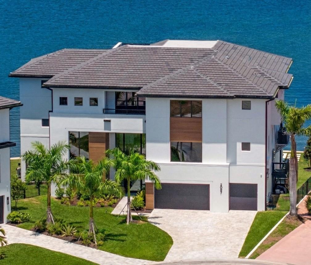 NEW PRICE: Positioned among Tampa Bay’s BEST VALUES for open-bay new construction luxury waterfront living, this residence is designed for those who expect the exceptional. Located in the Venetian Isles community, sweeping wide-bay views stretch across shimmering water to the Tampa Bay skyline. The professionally designed interior delivers sophisticated elegance and a curated coastal aesthetic, where warm Chesapeake hardwood floors and a serene palette of premium finishes welcome you inside. The expansive main living area is framed by floor-to-ceiling water views and anchored by a dramatic gas fireplace and architectural feature wall integrating a glass-enclosed wine cellar beside the formal dining space. A sleek chef’s kitchen showcases carbon-neutral Dekton countertops and backsplash, Thermador and Bosch appliances, and a full prep kitchen with additional dishwasher and refrigerator, complemented by an expansive waterfall island and seamless access to the main terrace with outdoor kitchen. The primary living level includes three ensuite guest bedrooms and one of two laundry rooms featuring LG appliances. Upstairs, a versatile bonus room is ideal for relaxing or entertaining with a custom wet bar and media wall, while expansive glass doors open to the waterfront terrace and spiral stair access leads to a rooftop terrace offering panoramic bay views. Through double doors, the private primary suite showcases spectacular water views, custom closets, and a spa-inspired bath with backlit mirrors, oversized glass shower, and deep soaking tub, along with a powder bath, an additional ensuite guest bedroom with walk-in closet, and the second laundry room. Outdoor living defines modern Florida coastal luxury with over 750 square feet of covered lanai space, a heated saltwater pool and spa overlooking the bay, and a private dock for year-round recreation. A 3-stop commercial-grade glass elevator, marine-grade outdoor cabinetry, dual laundry rooms, a 3-car garage, PGT impact windows and sliders, and impact garage doors complete this exceptional waterfront residence. Built on pilings for strength, stability, and lasting confidence, this modern waterfront home is ideally located with convenient access to parks, recreation, Gulf beaches, and downtown St. Petersburg’s vibrant arts and culinary scene.